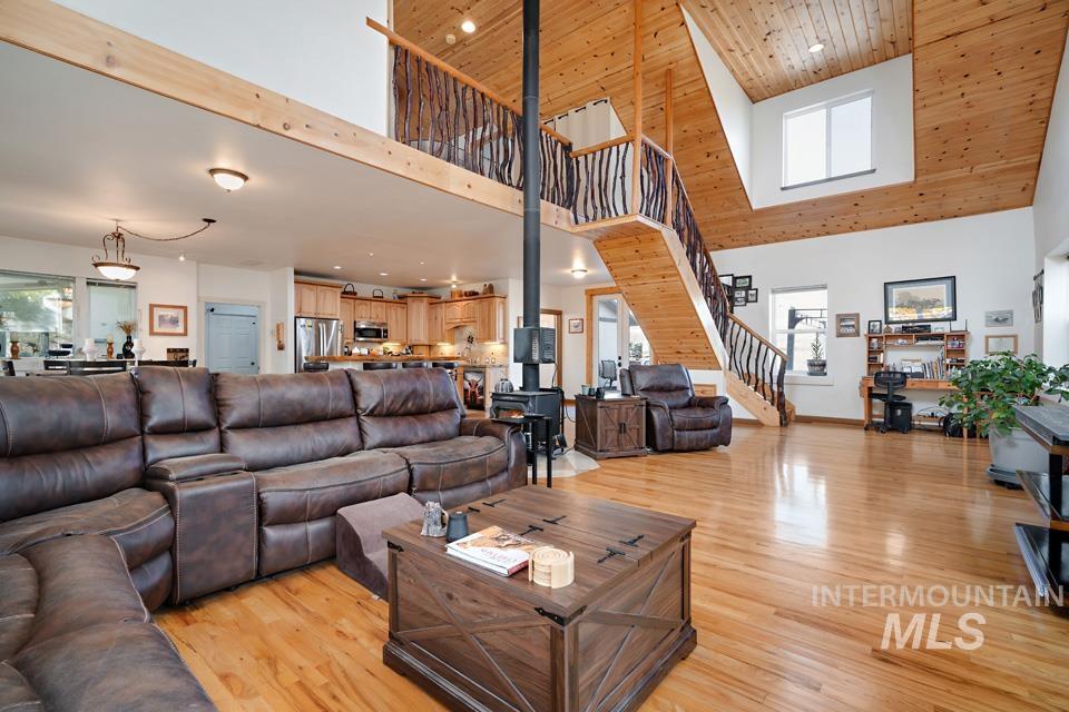 Living room featuring light wood-style floors, stairway, wooden ceiling, a high ceiling, and a wood stove