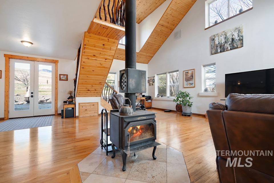 Living area featuring a wood stove, french doors, light wood-style flooring, and high vaulted ceiling