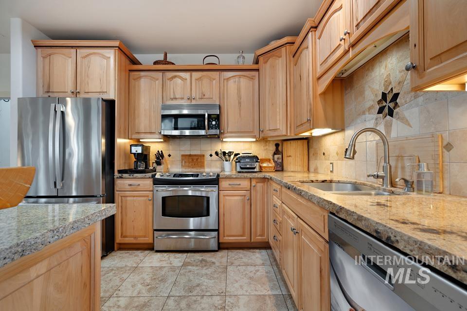 Kitchen with stainless steel appliances, backsplash, light brown cabinetry, and light stone counters