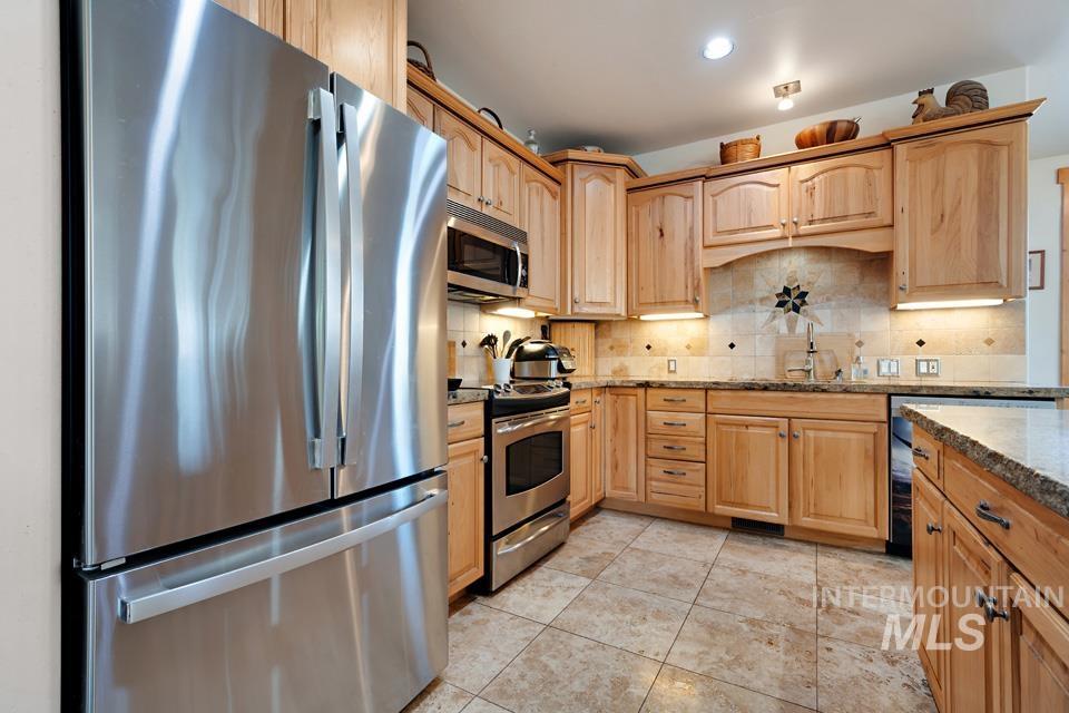 Kitchen featuring stainless steel appliances, light brown cabinets, dark stone countertops, recessed lighting, and tasteful backsplash