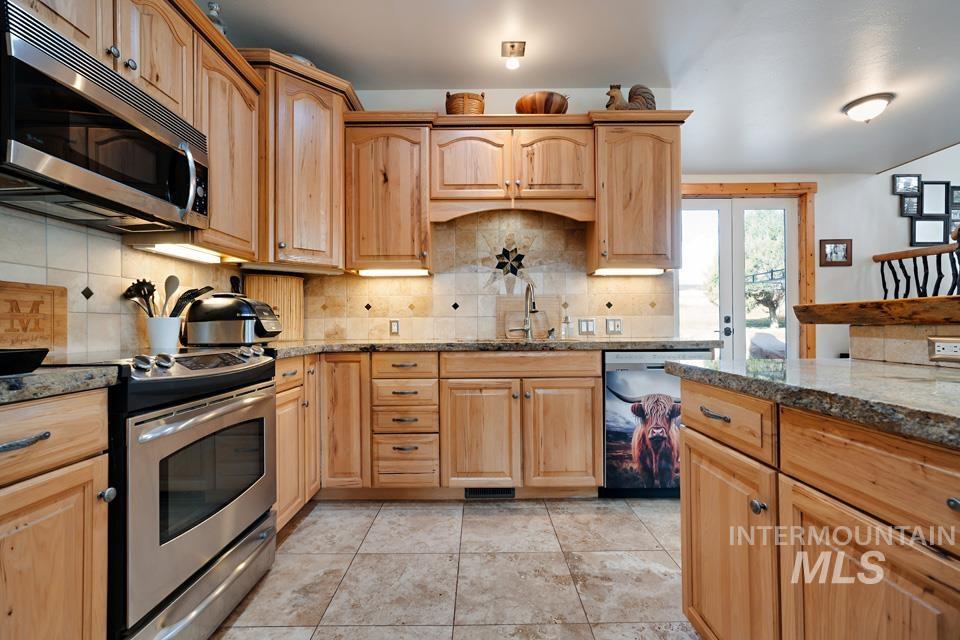 Kitchen featuring stainless steel appliances, decorative backsplash, dark stone counters, light brown cabinets, and french doors