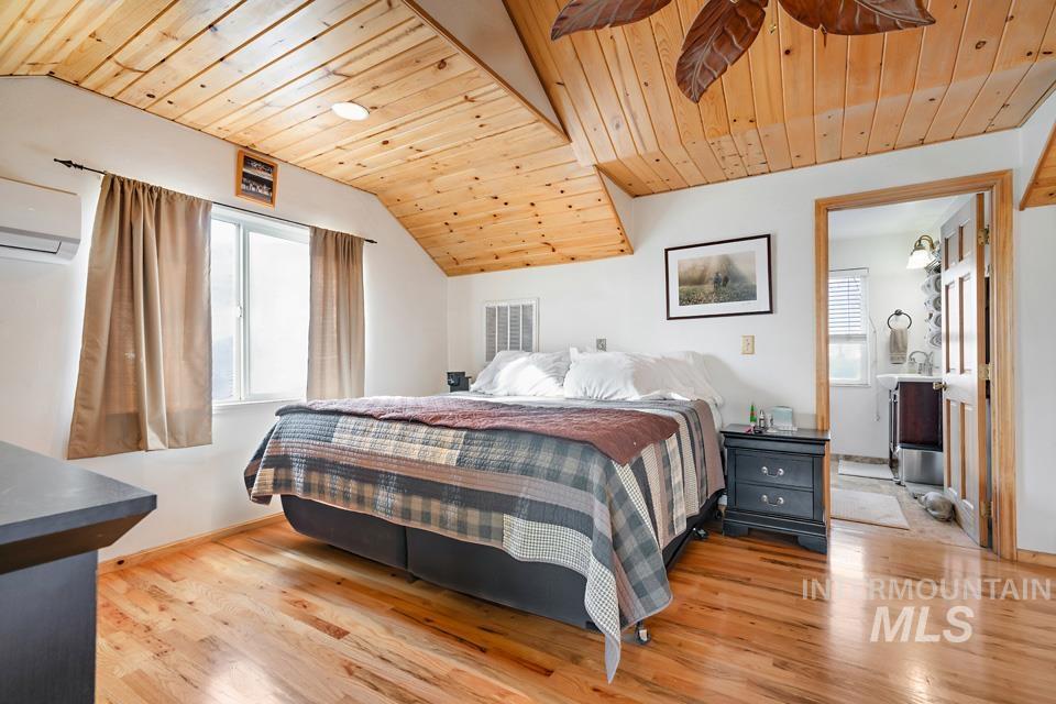 Bedroom featuring wooden ceiling, light wood-style floors, multiple windows, vaulted ceiling, and a wall unit AC