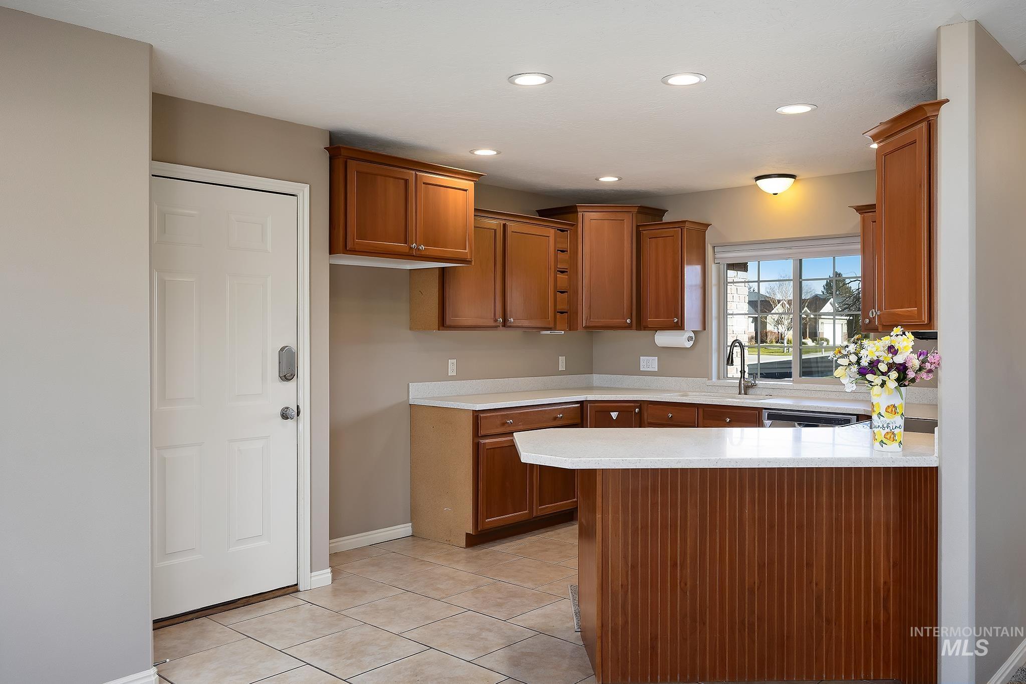Kitchen featuring brown cabinetry, a peninsula, recessed lighting, light tile patterned floors, and light stone countertops