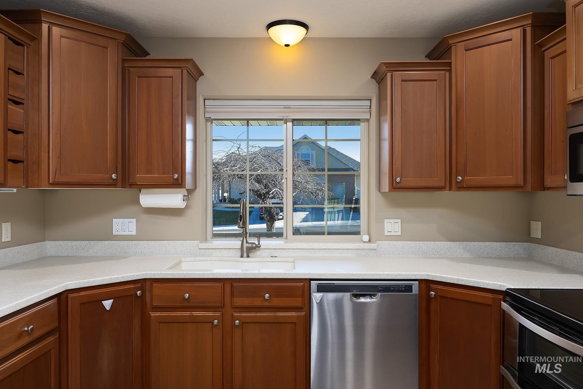 Kitchen featuring stainless steel appliances, brown cabinets, and light stone countertops