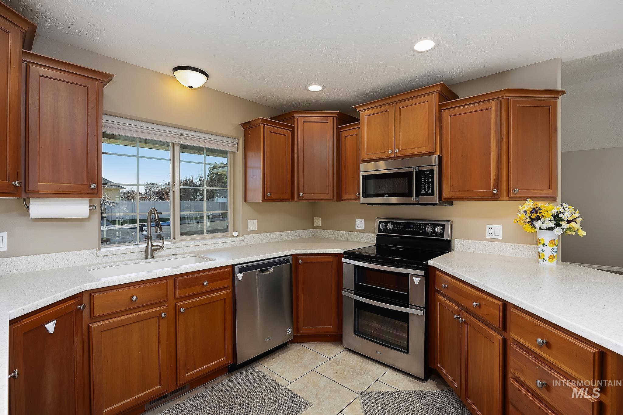 Kitchen with appliances with stainless steel finishes, brown cabinetry, light stone counters, light tile patterned floors, and recessed lighting