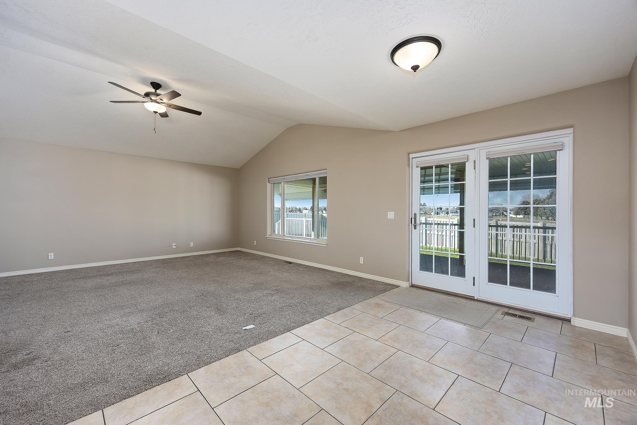 Empty room featuring light colored carpet, vaulted ceiling, a ceiling fan, and light tile patterned flooring