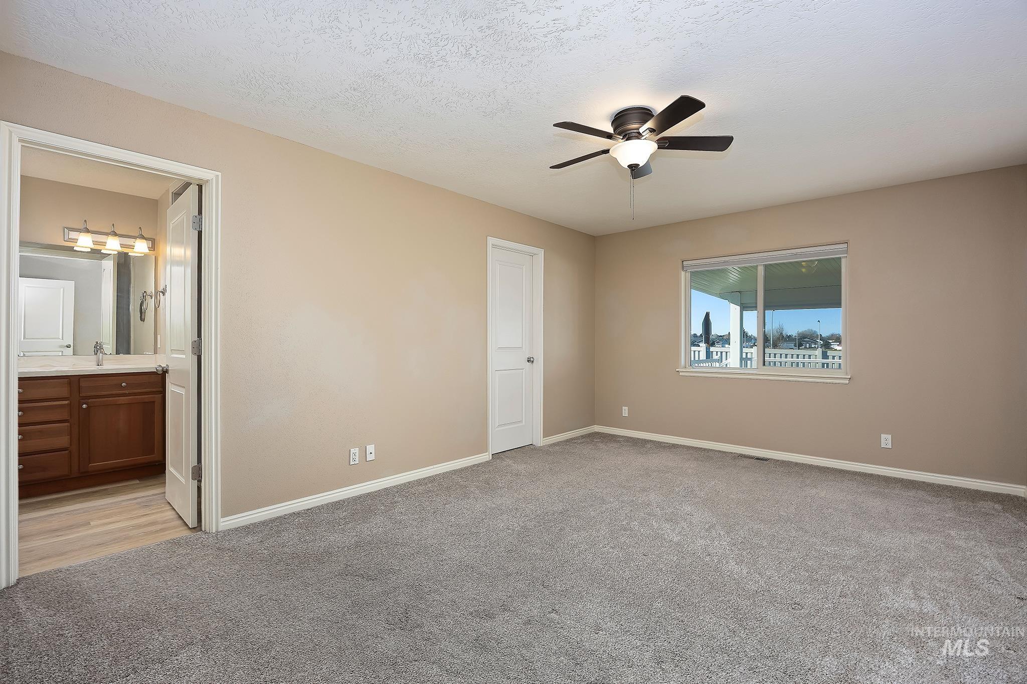 Unfurnished bedroom with light carpet, a textured ceiling, a ceiling fan, and connected bathroom