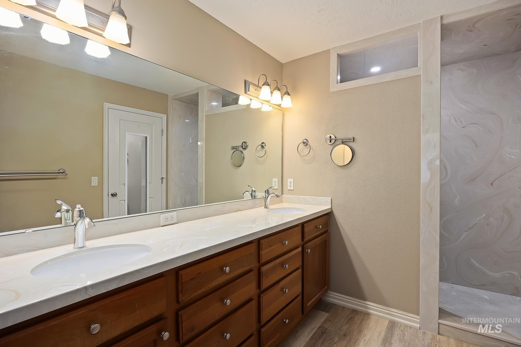 Bathroom with double vanity, light wood finished floors, and a shower