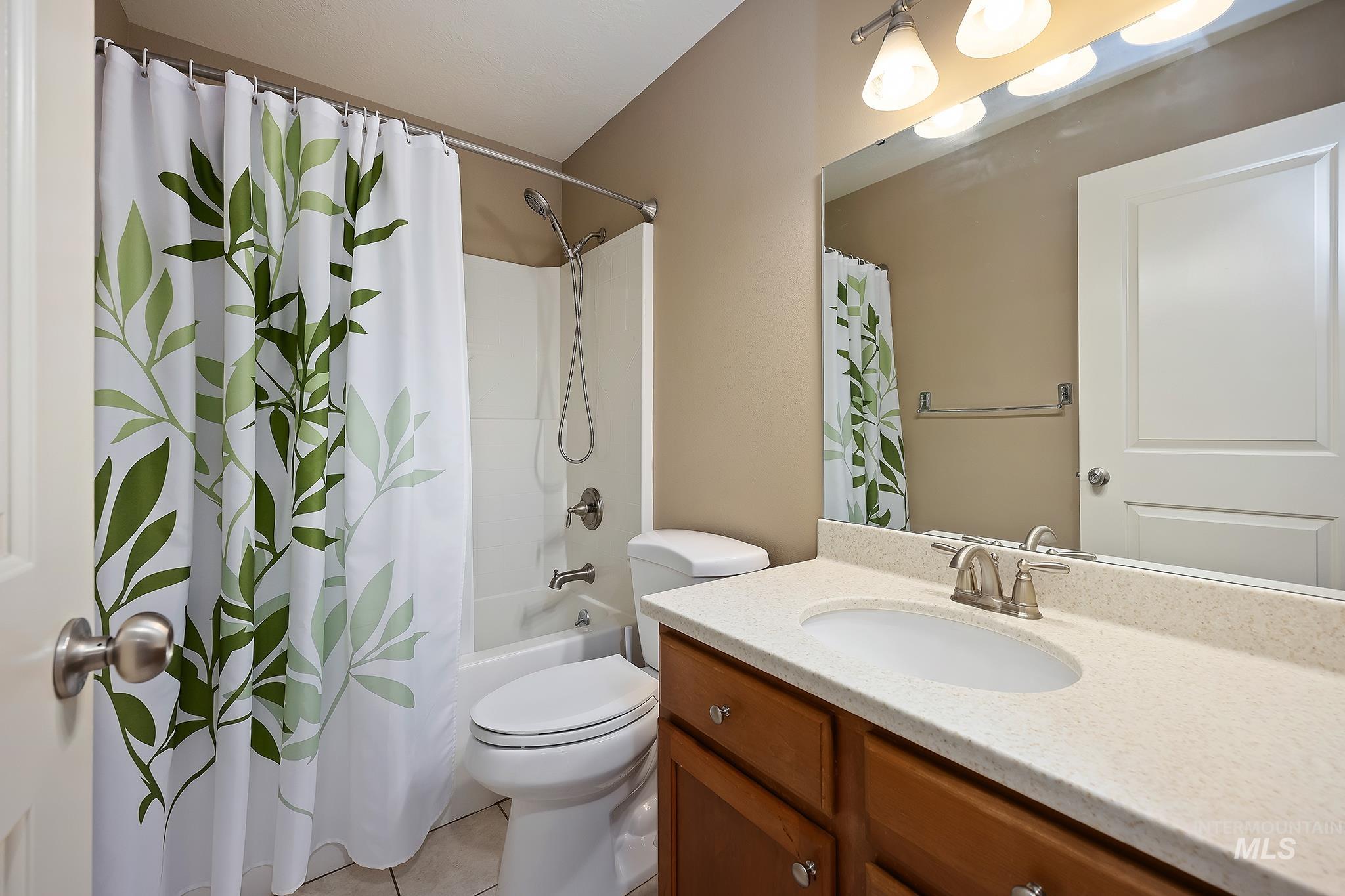 Full bath featuring vanity, shower / tub combo with curtain, and light tile patterned floors