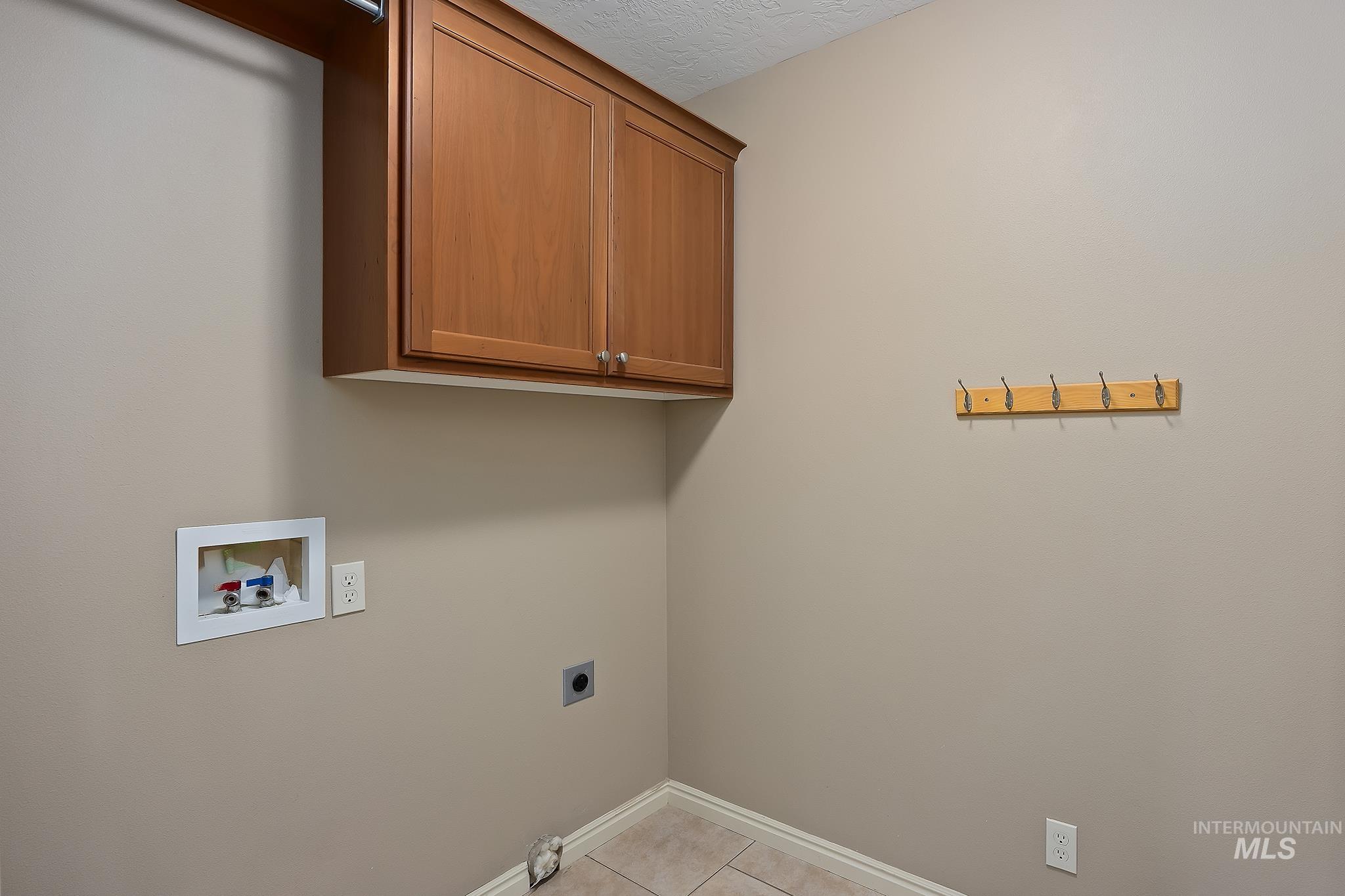Laundry room featuring cabinet space, hookup for a washing machine, light tile patterned flooring, hookup for an electric dryer, and a textured ceiling