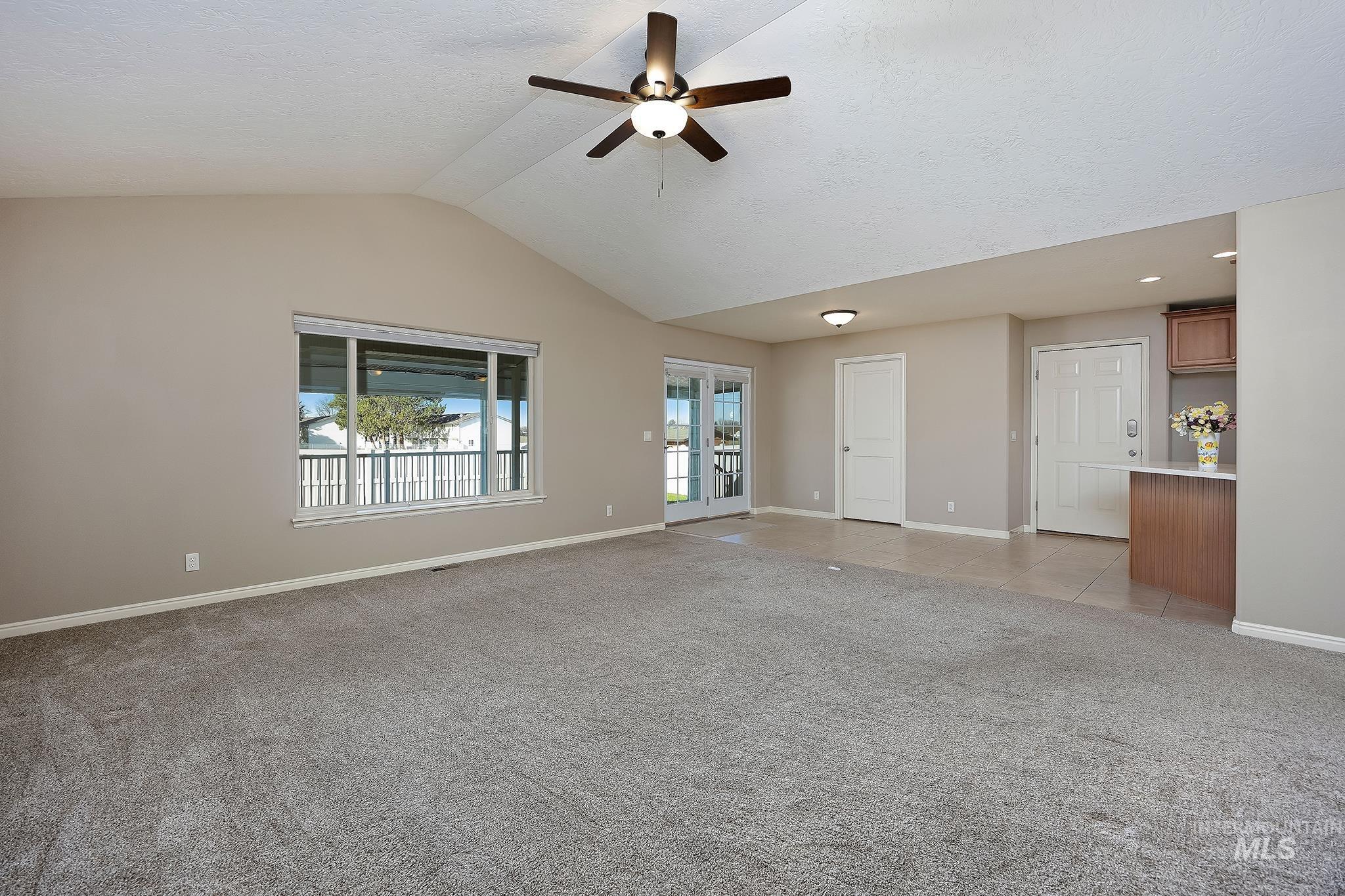 Unfurnished living room with light colored carpet, ceiling fan, and lofted ceiling