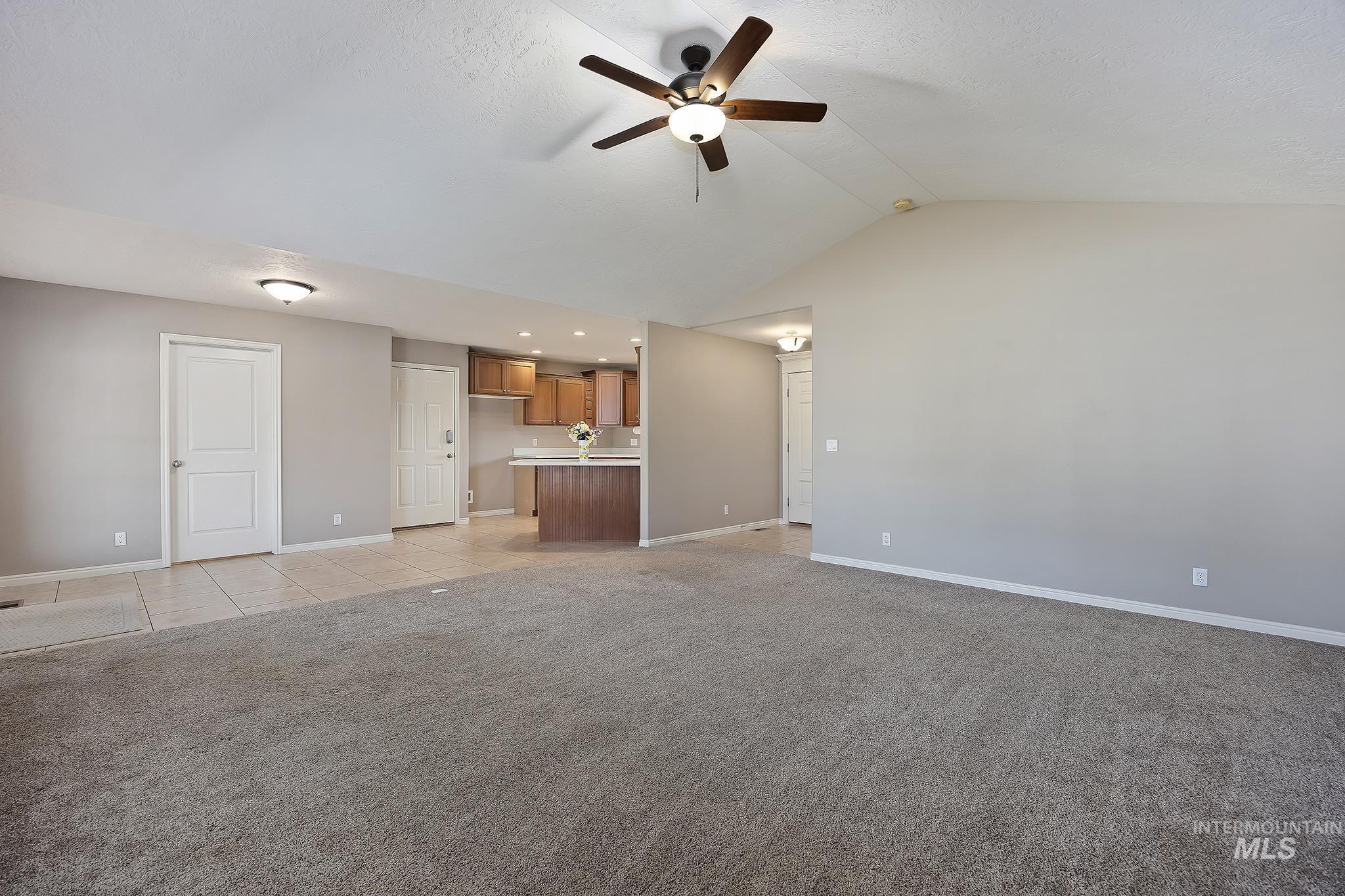 Unfurnished living room with vaulted ceiling, ceiling fan, light tile patterned floors, and light carpet