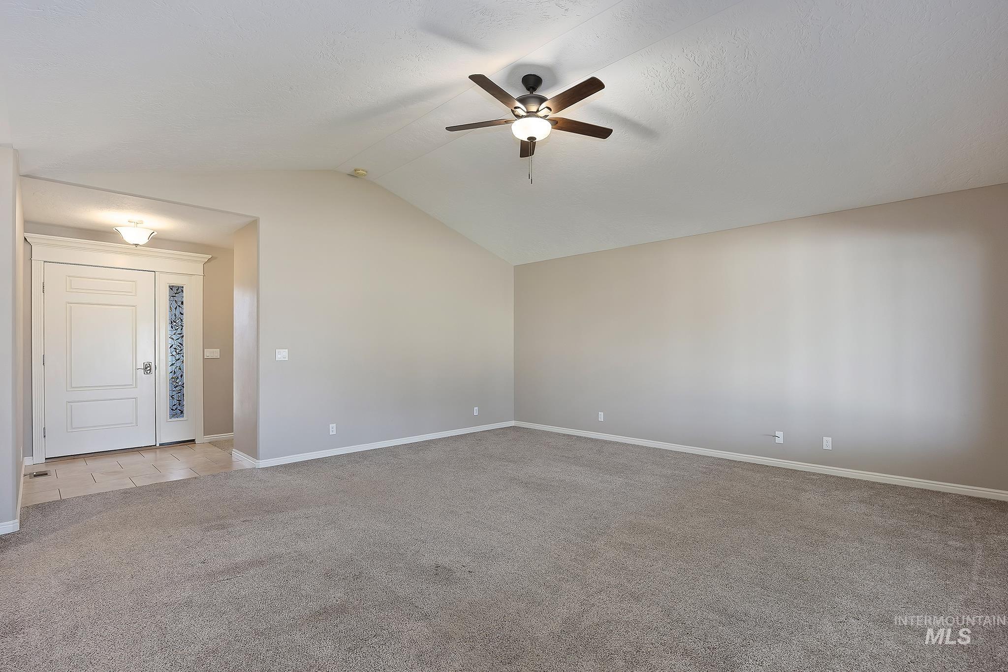 Empty room with lofted ceiling, light carpet, and ceiling fan