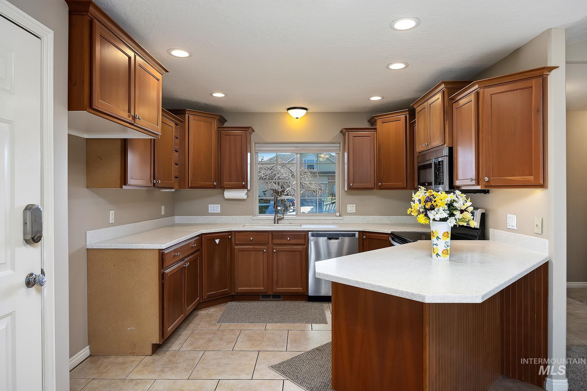 Kitchen featuring brown cabinets, a peninsula, appliances with stainless steel finishes, recessed lighting, and light tile patterned floors
