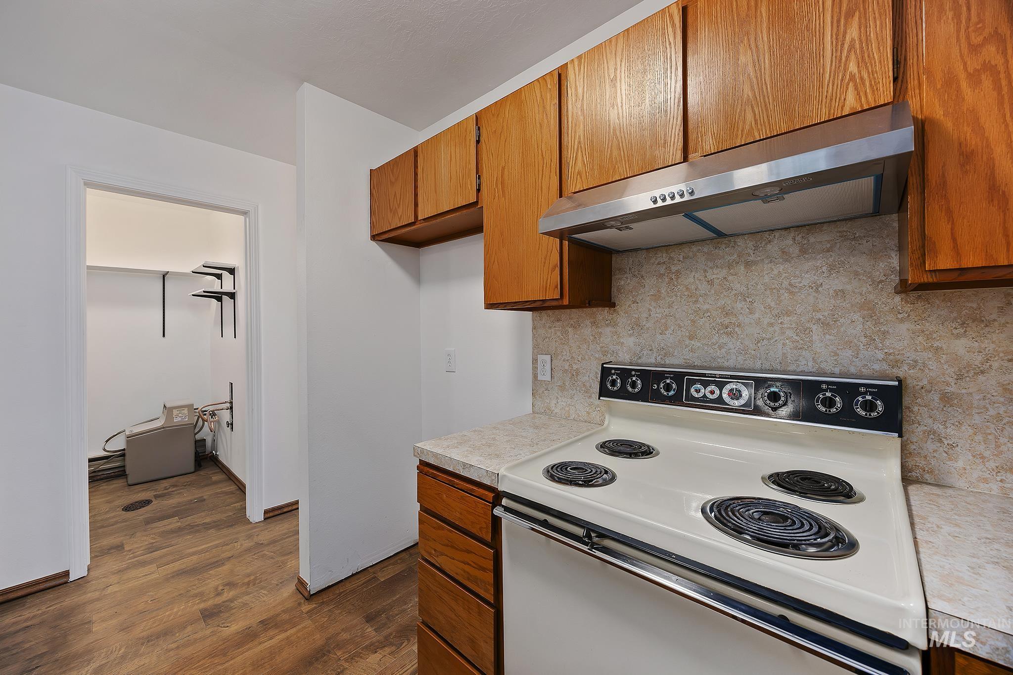 Kitchen featuring white range with electric stovetop, brown cabinetry, under cabinet range hood, and decorative backsplash