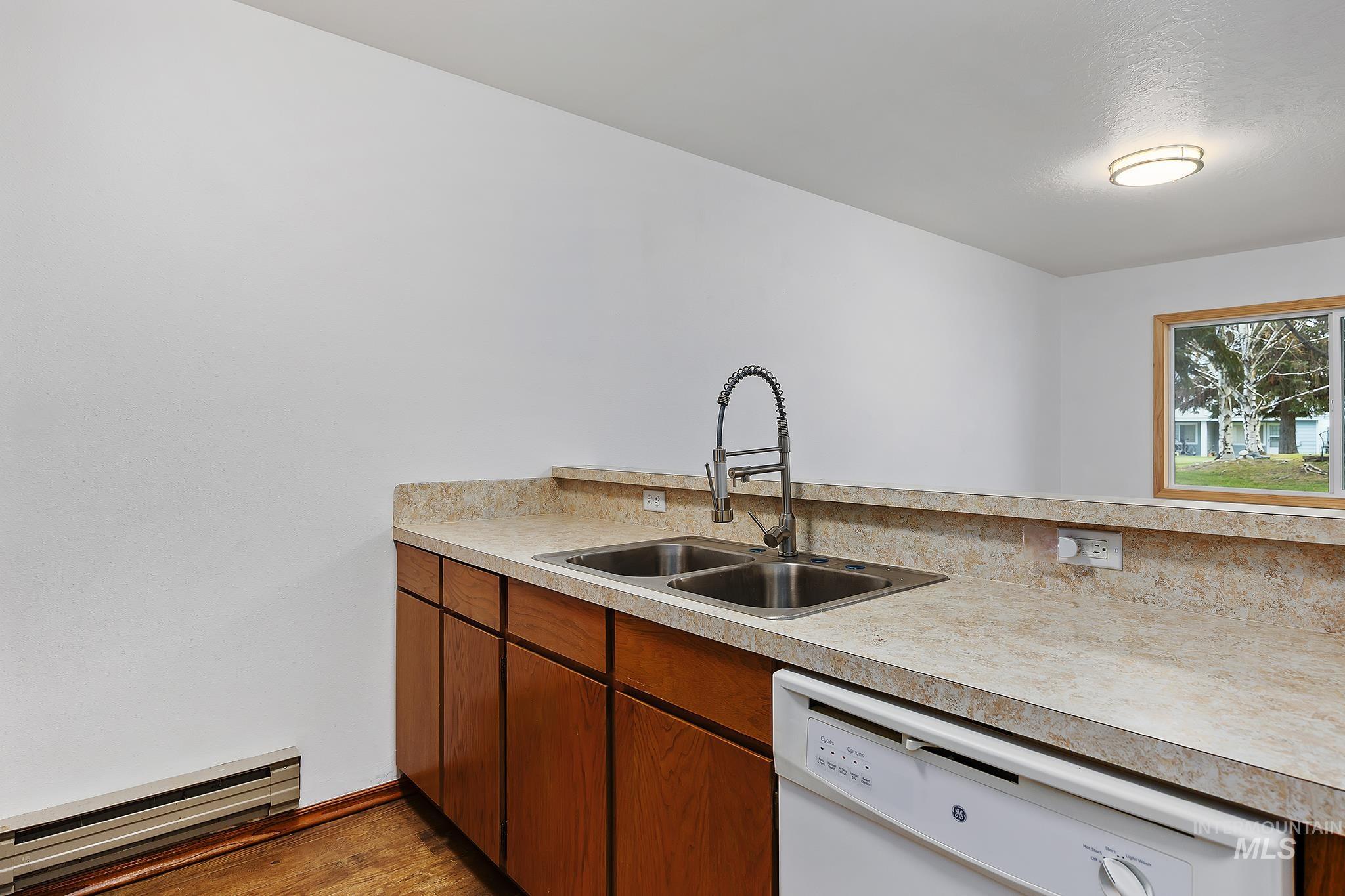 Kitchen with brown cabinets, a baseboard radiator, white dishwasher, and light countertops