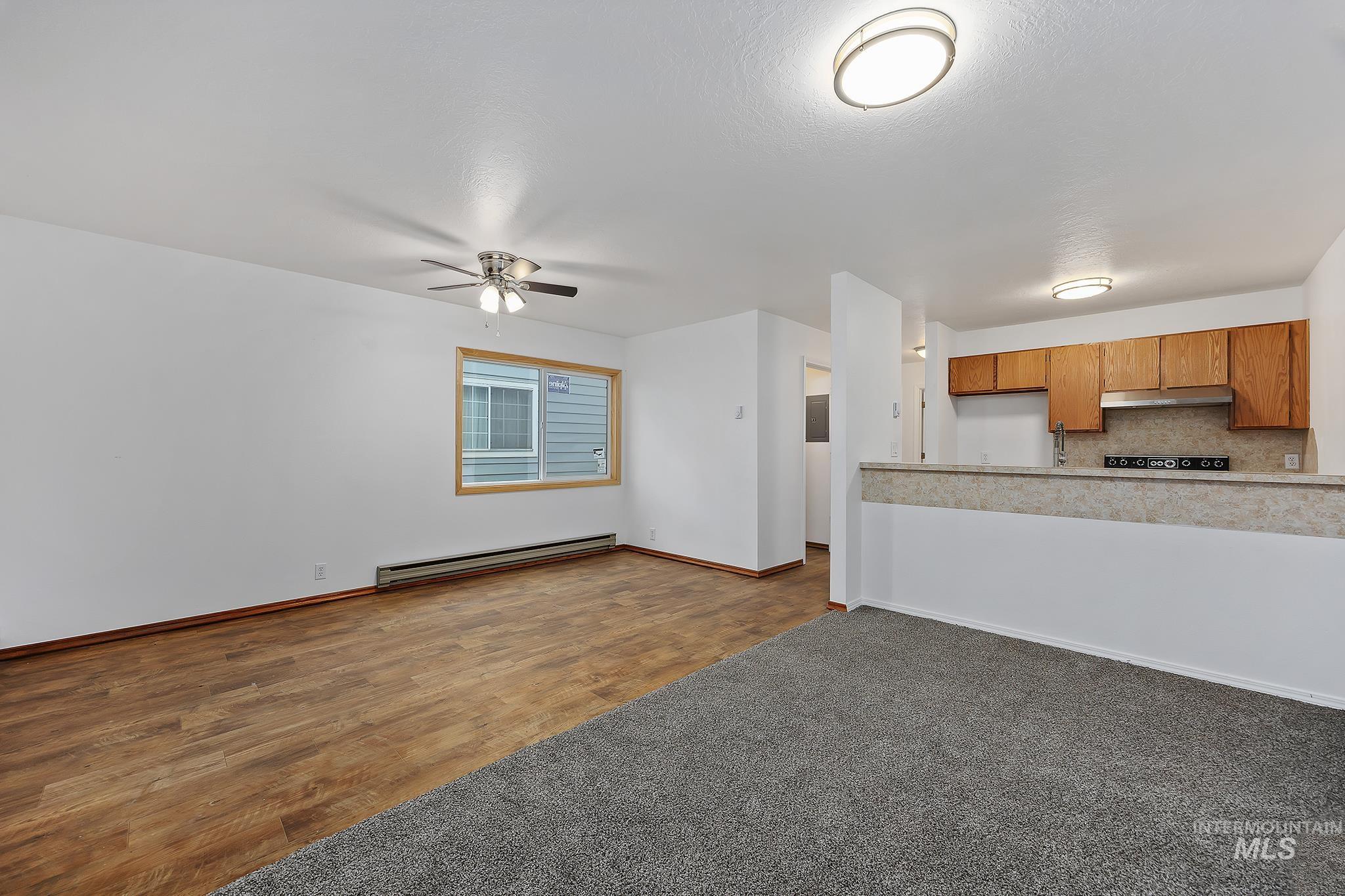 Unfurnished living room featuring a baseboard heating unit, dark wood-type flooring, and a ceiling fan