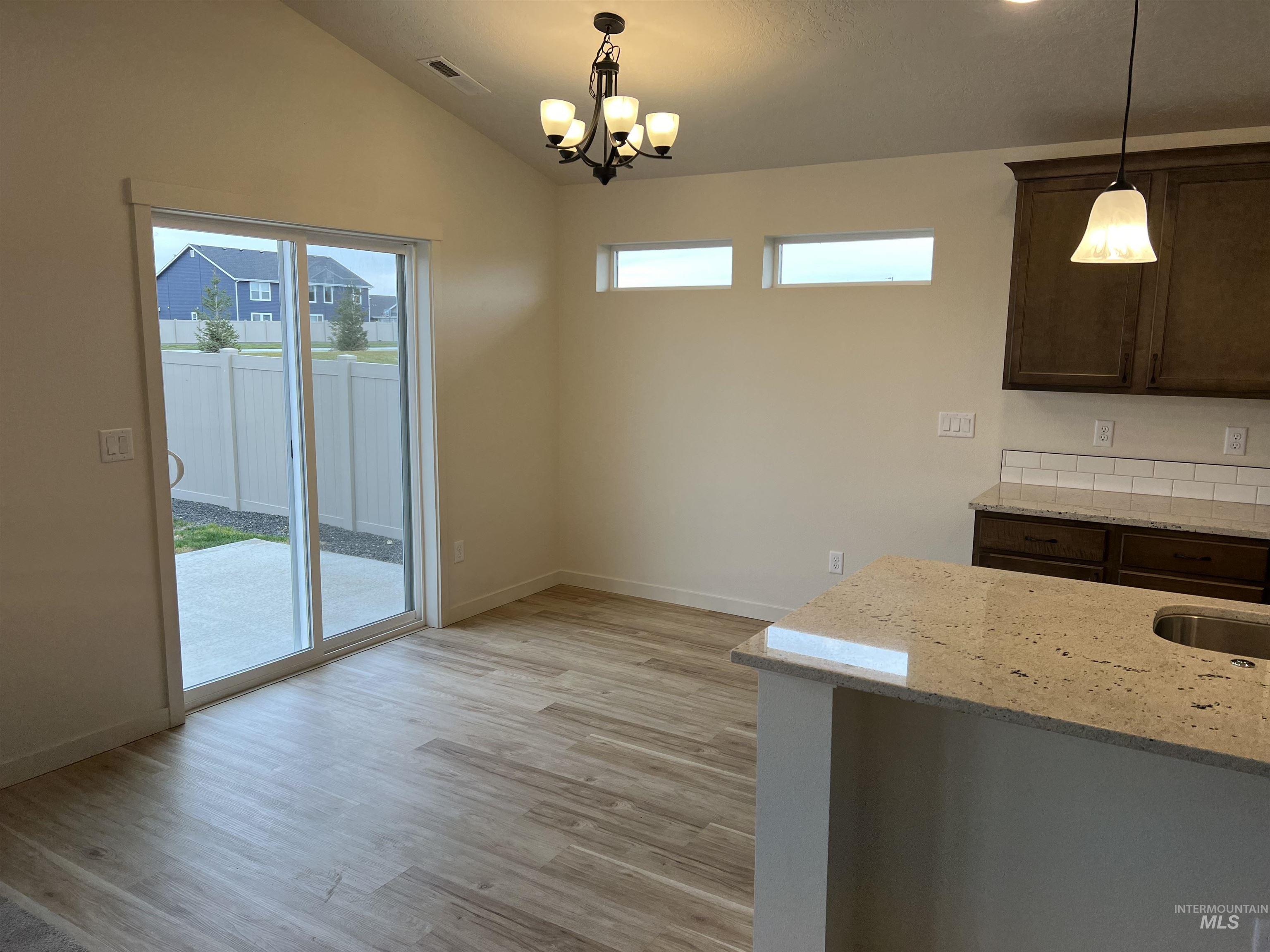 Unfurnished dining area with plenty of natural light, light wood-style flooring, vaulted ceiling, and a chandelier