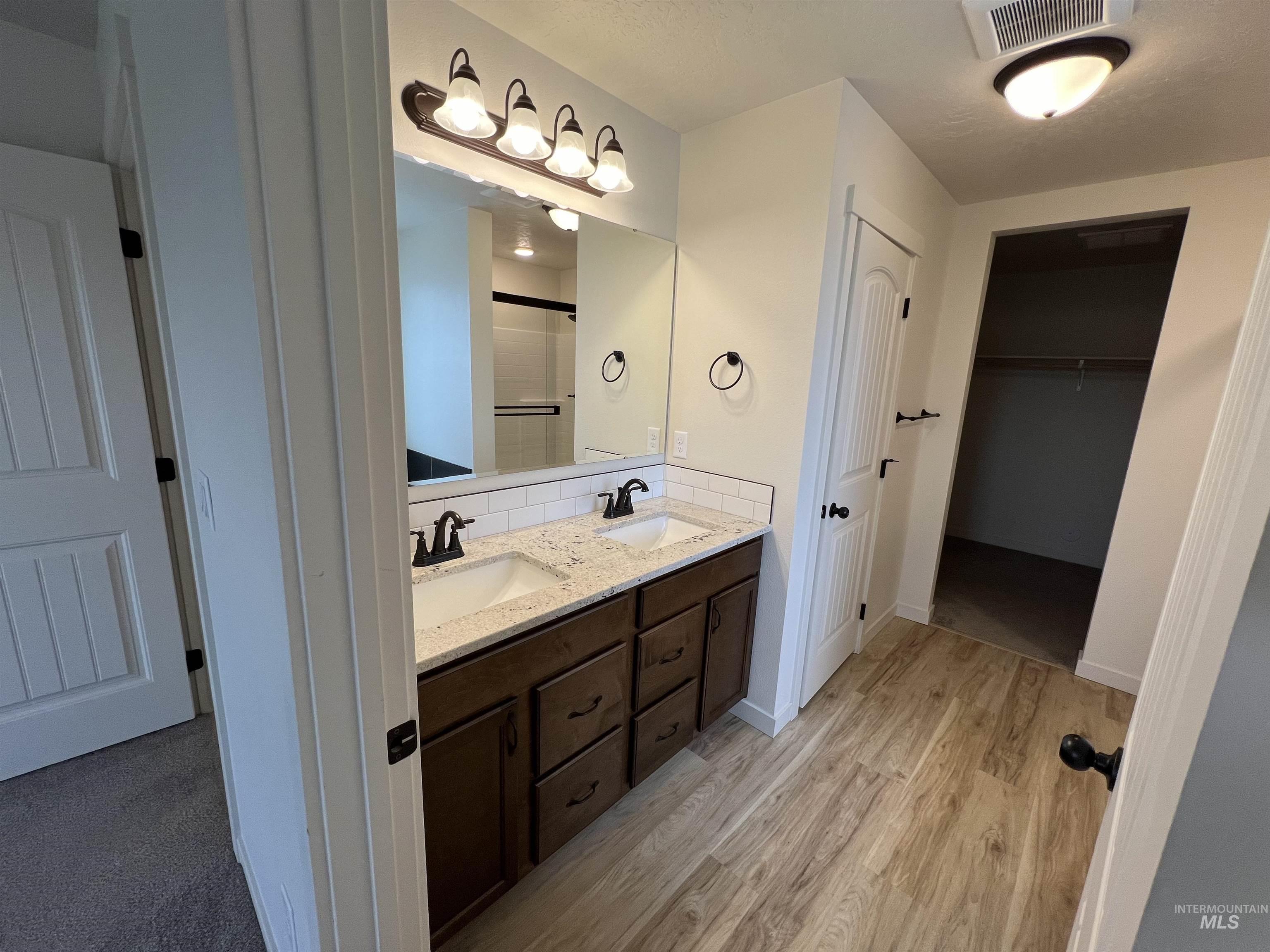 Bathroom with a spacious closet, double vanity, an enclosed shower, light wood finished floors, and a textured ceiling