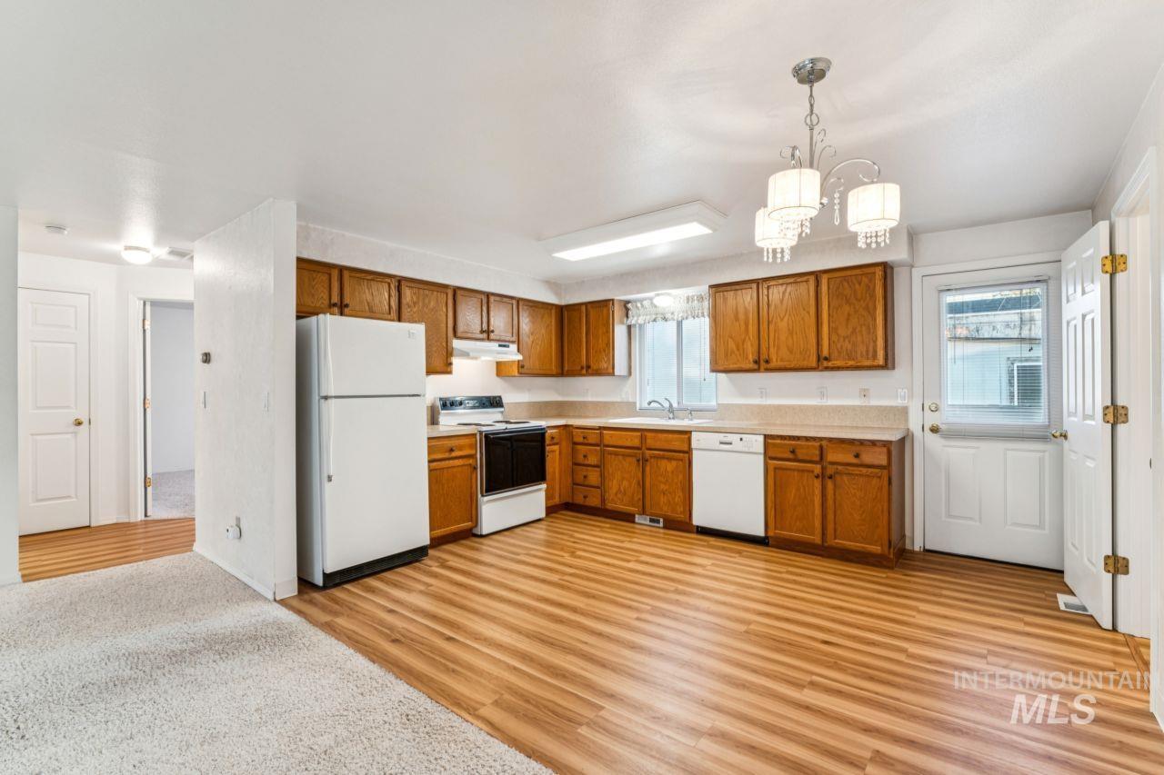 Kitchen with white appliances, brown cabinets, light countertops, light wood finished floors, and decorative light fixtures
