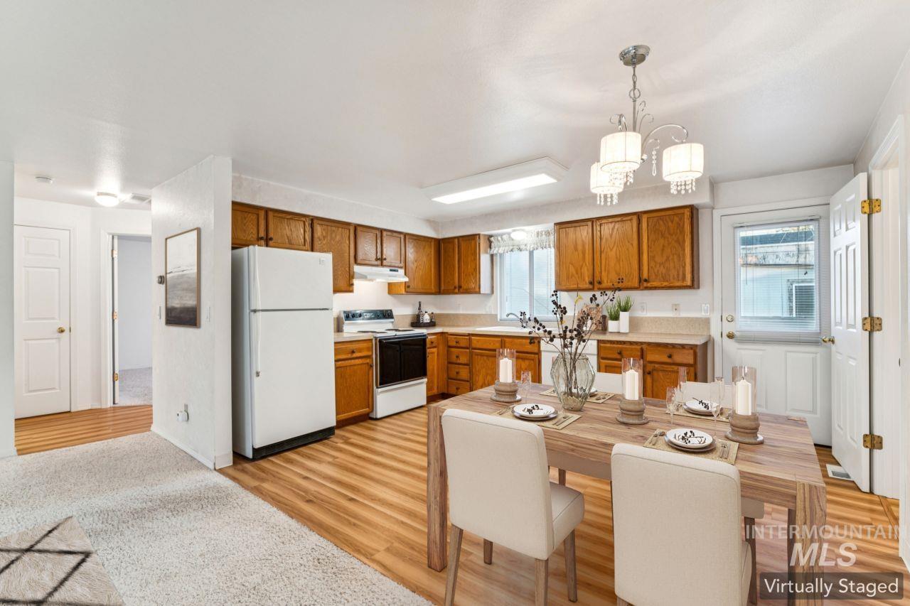 Kitchen featuring light countertops, white appliances, brown cabinetry, decorative light fixtures, and light wood-style floors