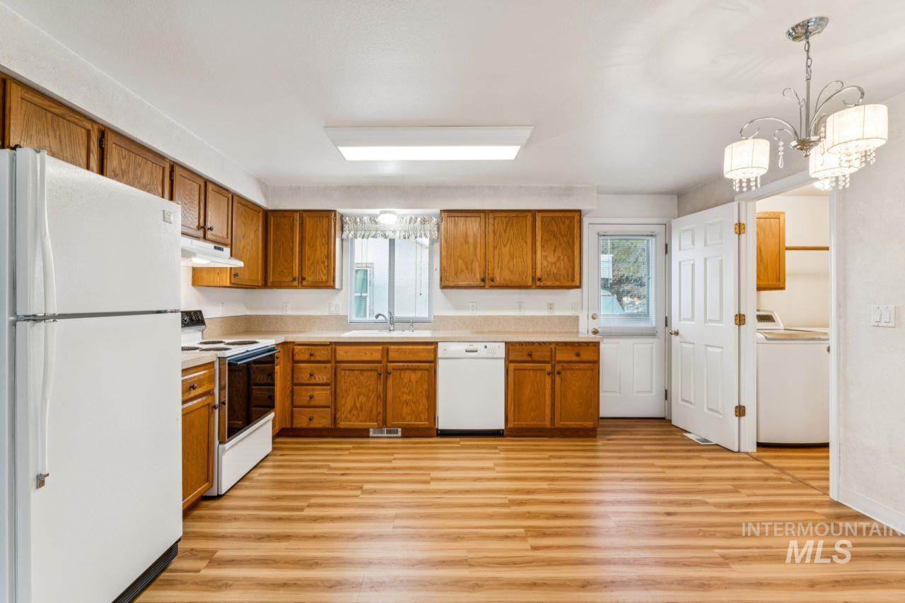 Kitchen featuring white appliances, light countertops, brown cabinetry, washer / dryer, and light wood-style flooring