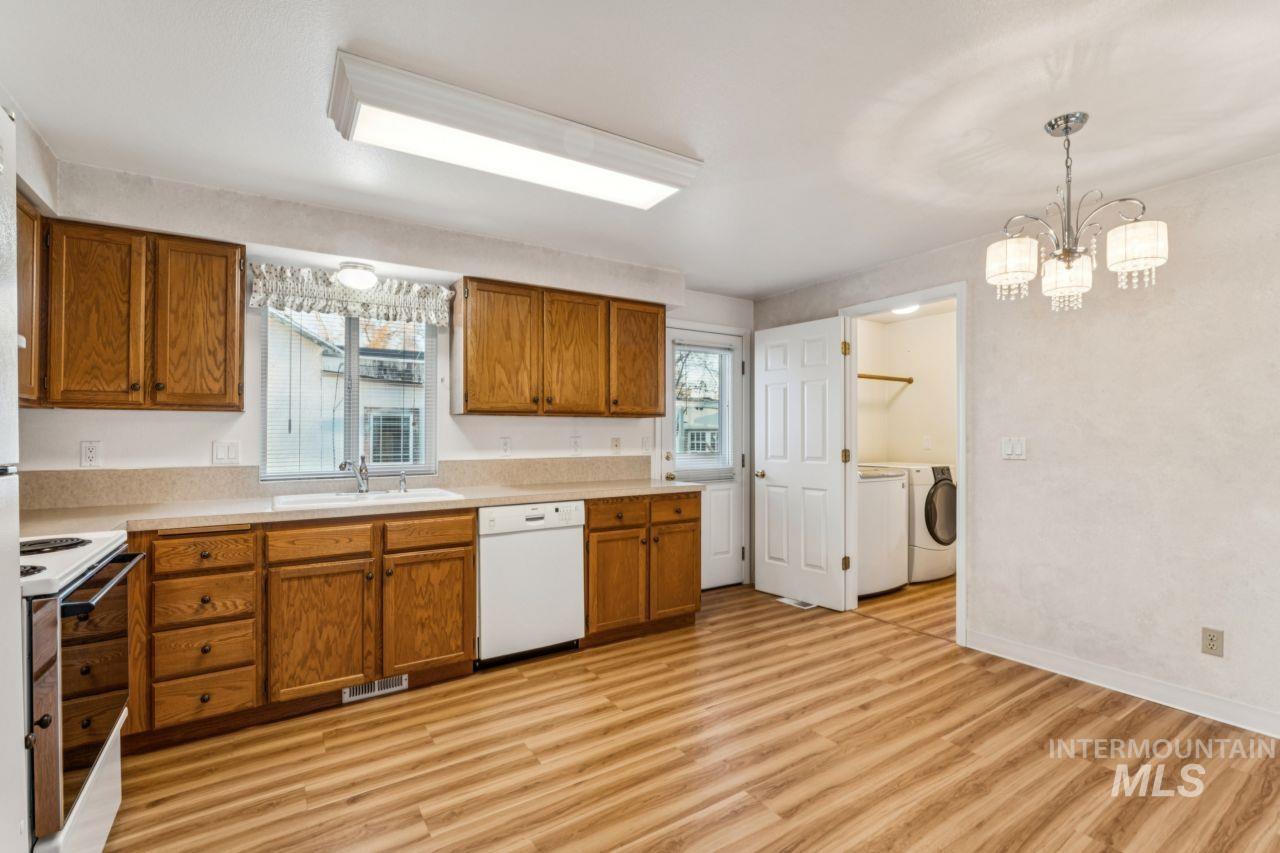 Kitchen featuring brown cabinets, light countertops, white appliances, and hanging light fixtures