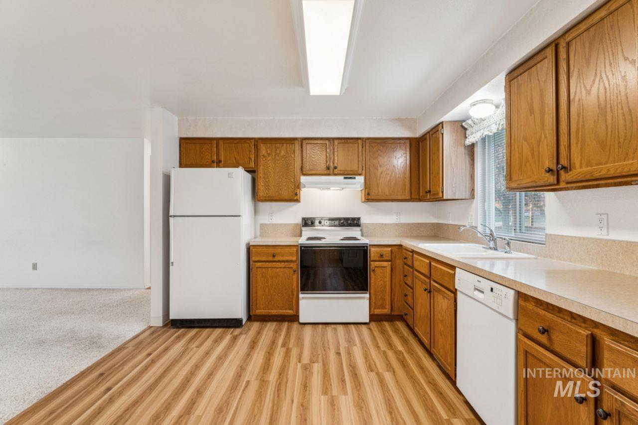 Kitchen featuring brown cabinets, white appliances, light countertops, and under cabinet range hood