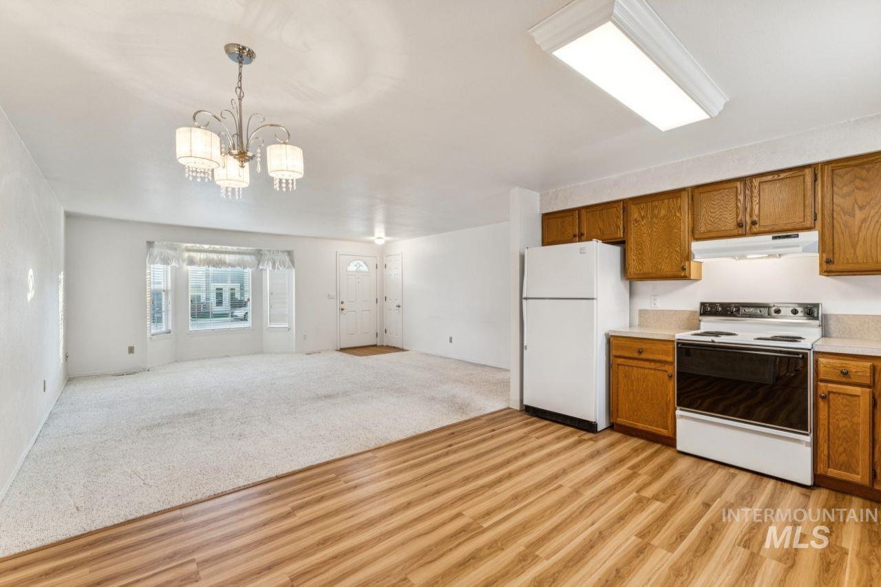 Kitchen featuring white appliances, brown cabinets, open floor plan, light countertops, and light carpet