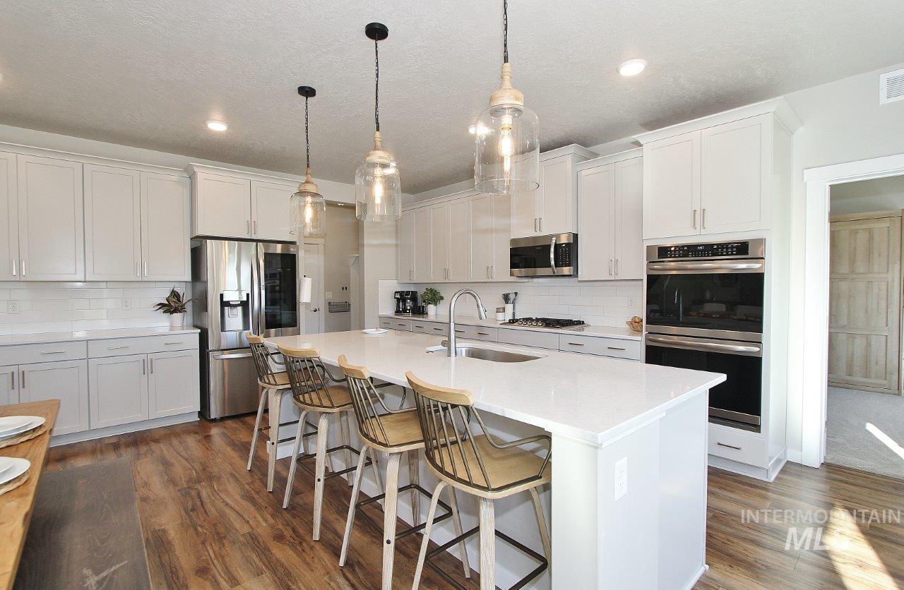 Kitchen featuring a kitchen breakfast bar, appliances with stainless steel finishes, decorative light fixtures, a kitchen island with sink, and dark wood-type flooring