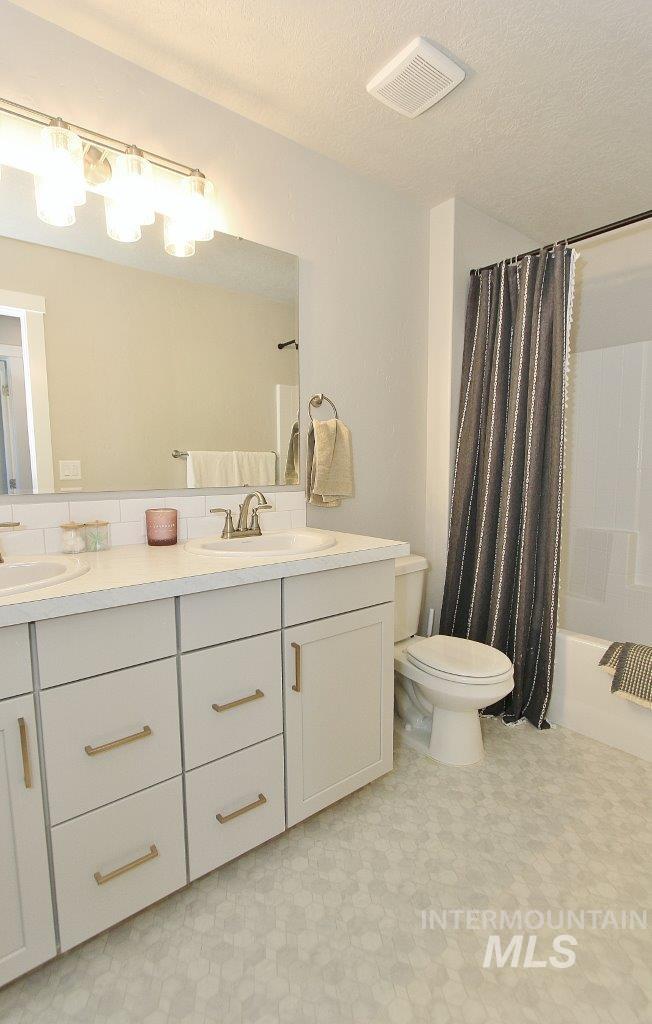 Bathroom with shower / tub combo, double vanity, light flooring, and a textured ceiling