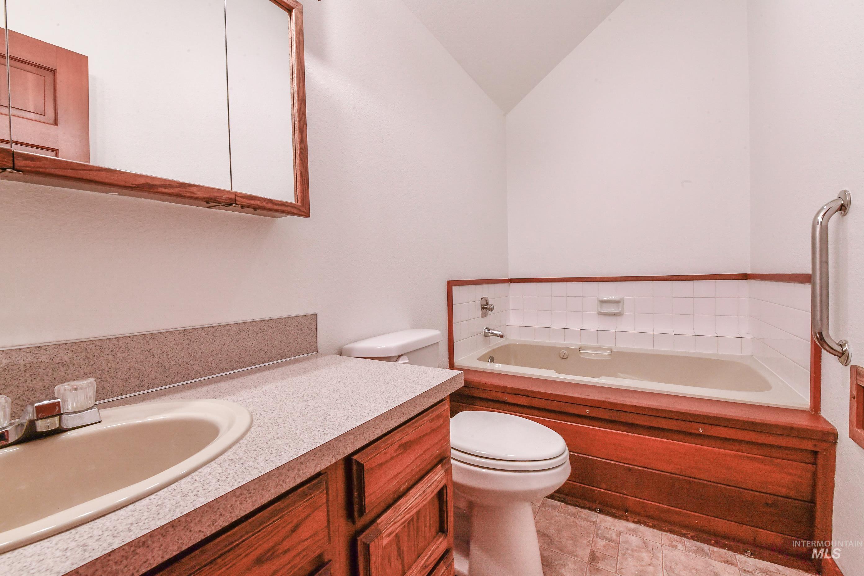 Full bathroom featuring a garden tub, vanity, and vaulted ceiling
