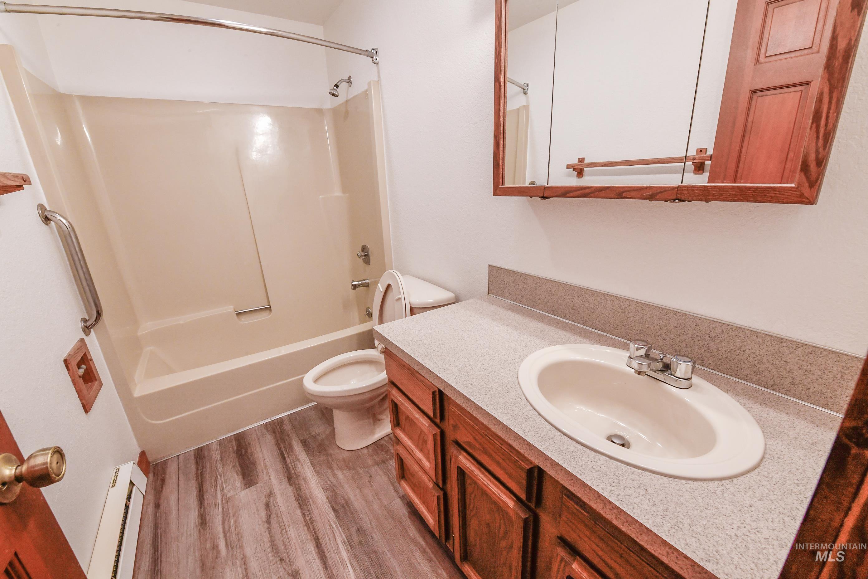 Full bathroom featuring a baseboard heating unit, wood finished floors, vanity, and shower / bath combination