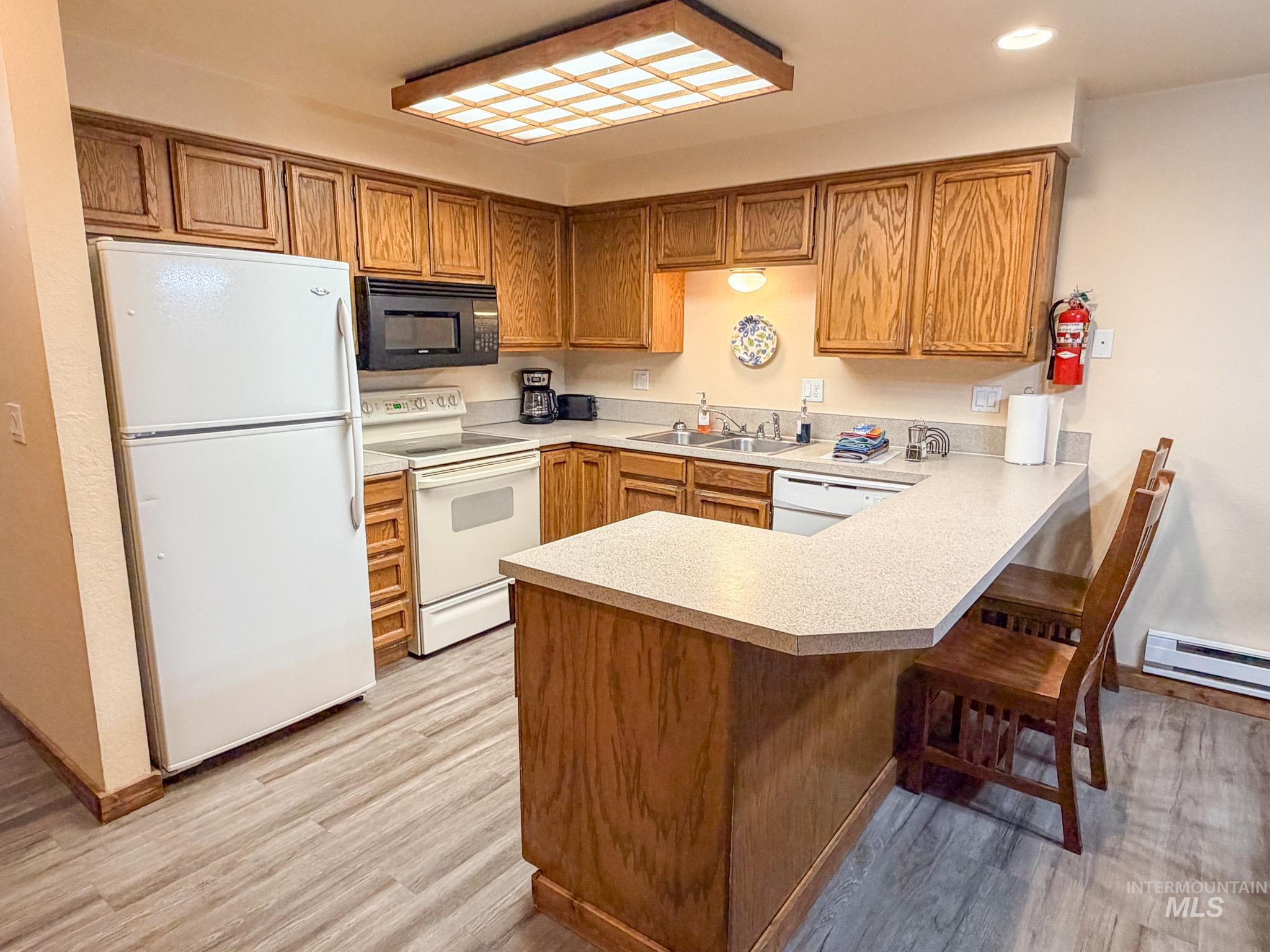 Kitchen featuring white appliances, a peninsula, light countertops, a kitchen breakfast bar, and brown cabinetry