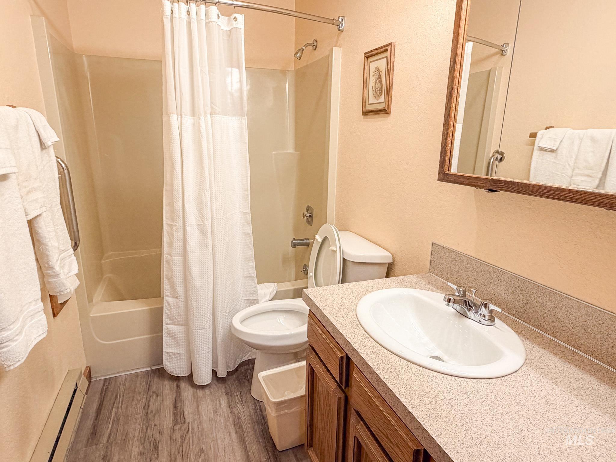 Bathroom featuring shower / tub combo with curtain, vanity, a baseboard heating unit, a textured wall, and dark wood-style floors