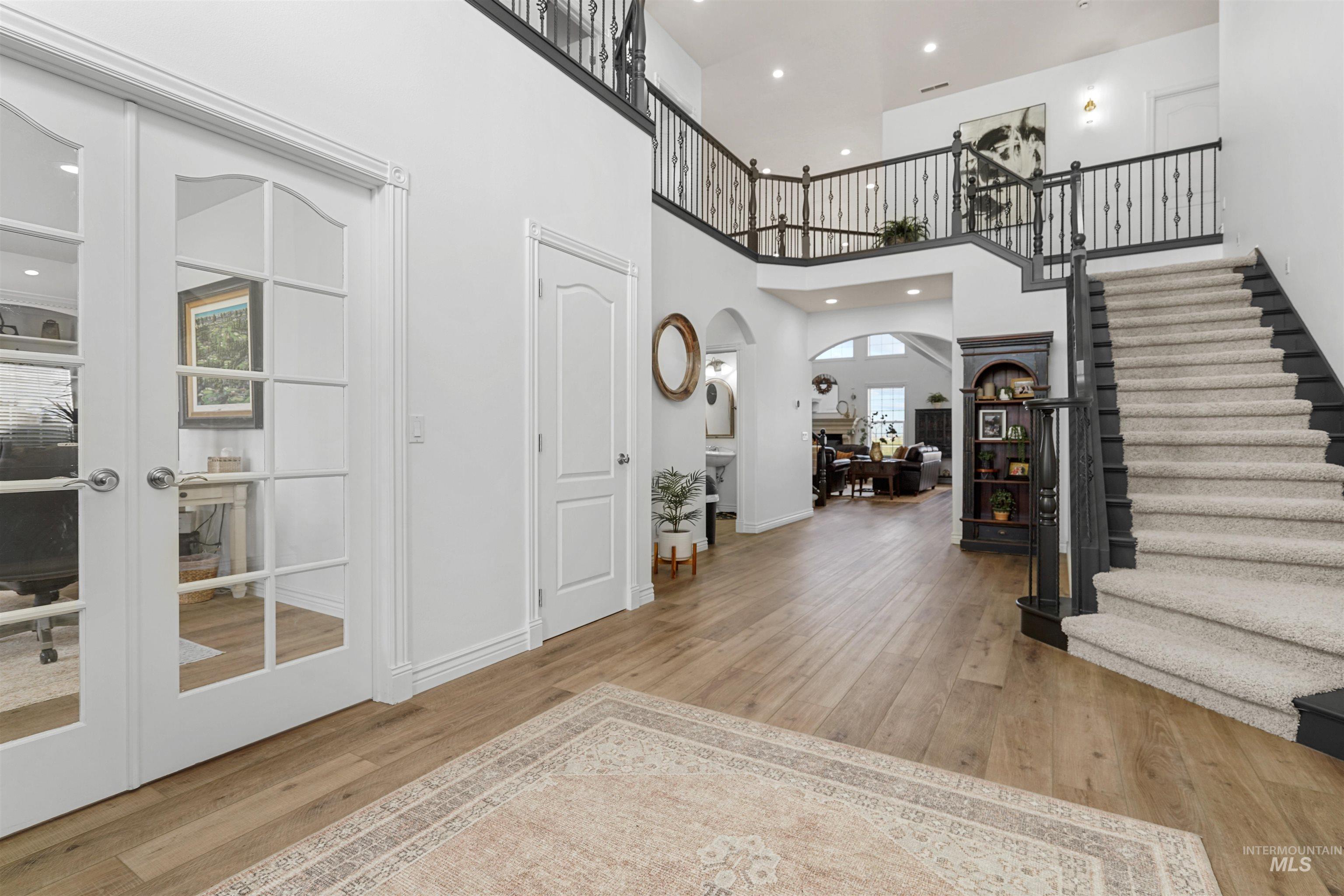 Foyer featuring a high ceiling, light wood finished floors, arched walkways, stairway, and recessed lighting