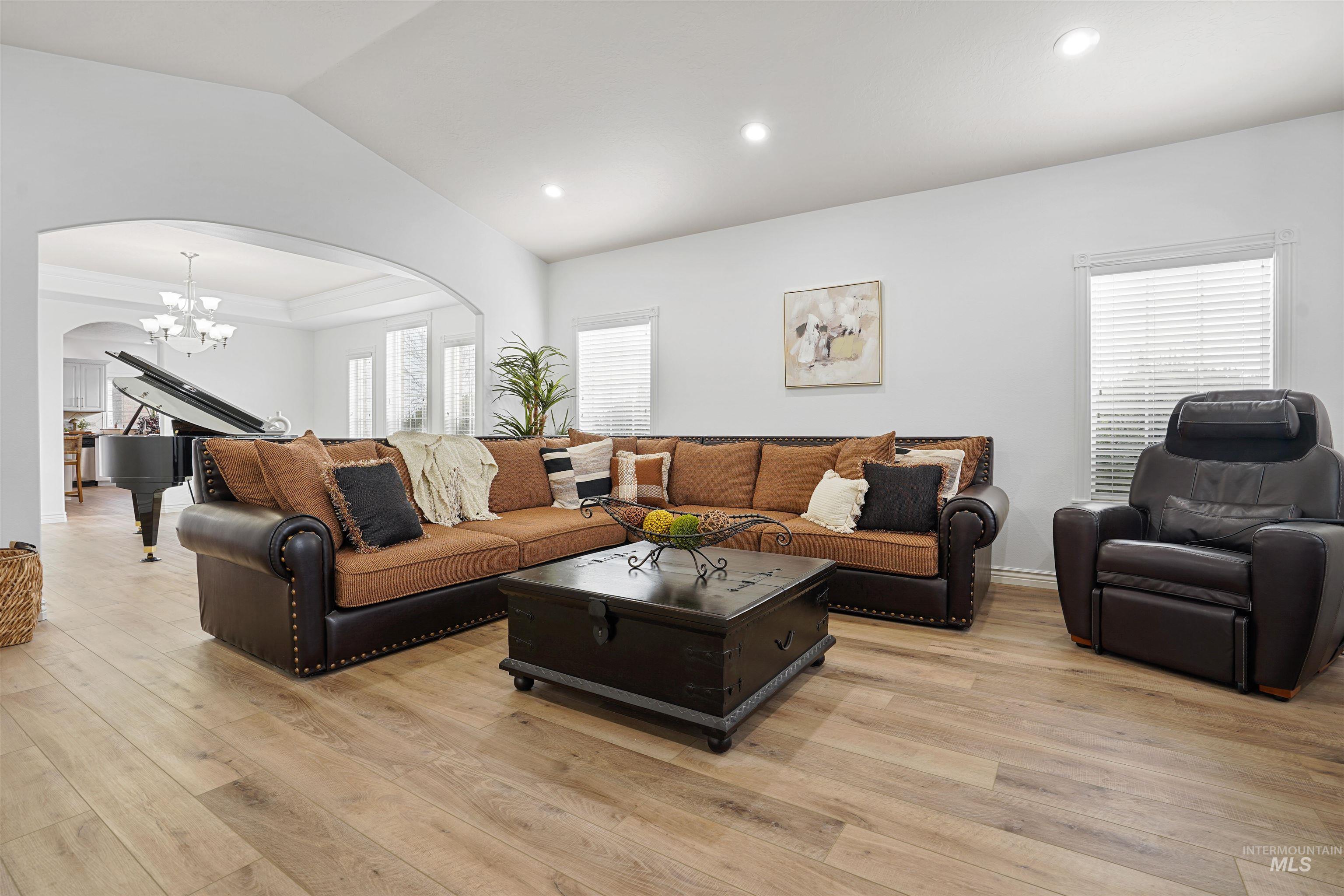 Living room with arched walkways, a chandelier, light wood-style flooring, vaulted ceiling, and recessed lighting