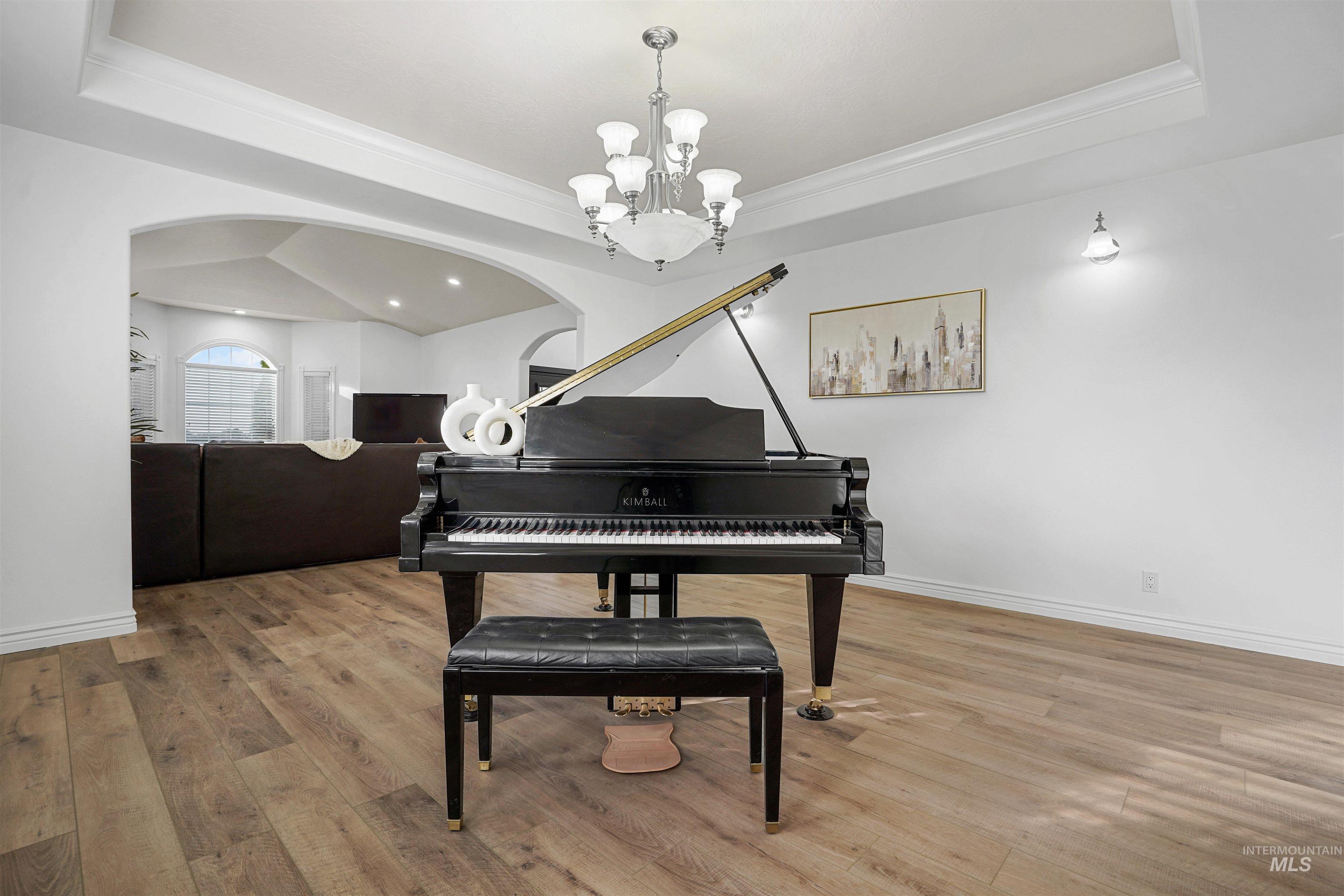 Living area featuring a raised ceiling, light wood finished floors, ornamental molding, and arched walkways