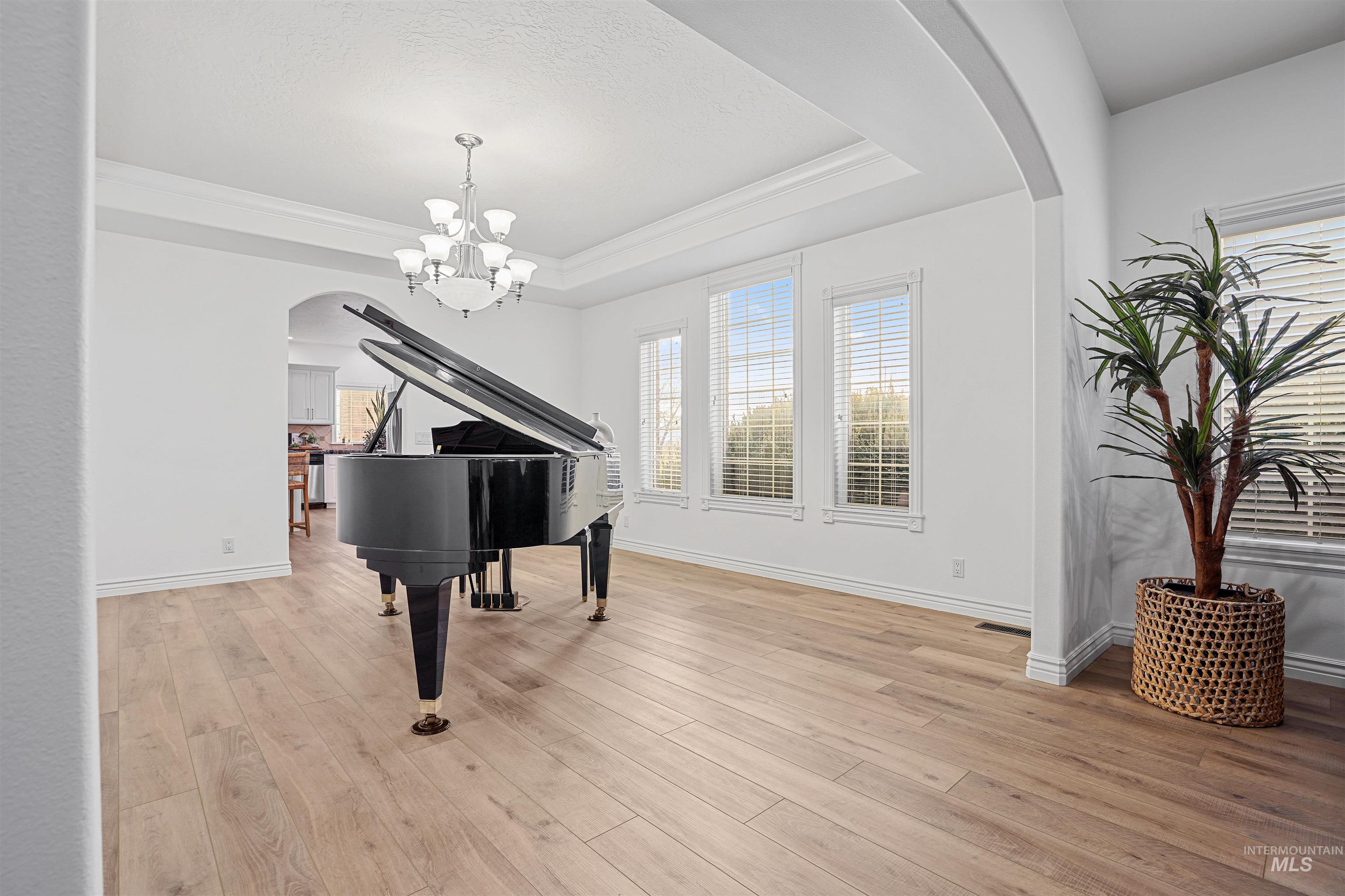 Living area with arched walkways, light wood-style floors, a tray ceiling, ornamental molding, and a chandelier