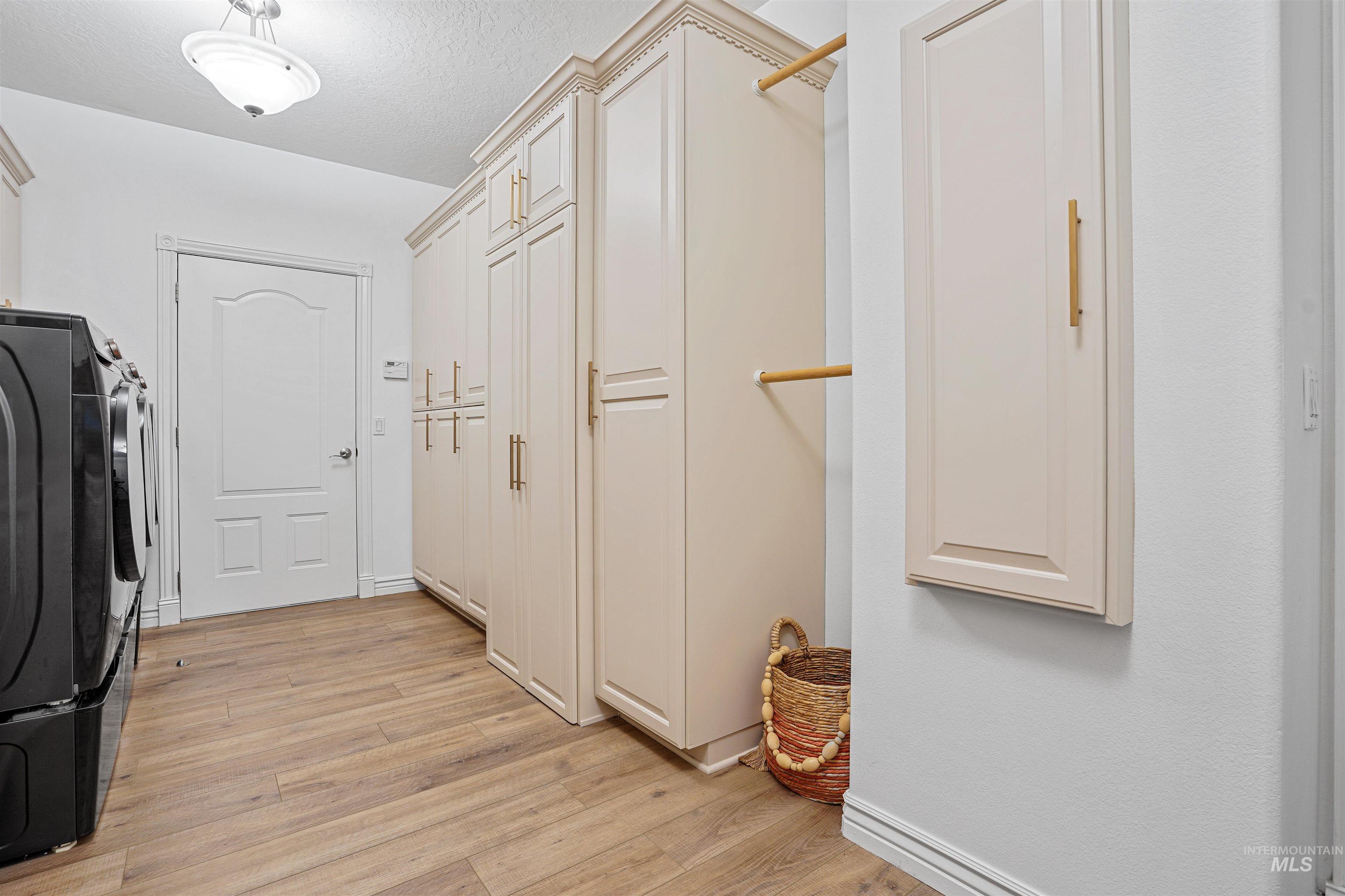 Washroom with light wood finished floors, washer and dryer, and a textured ceiling