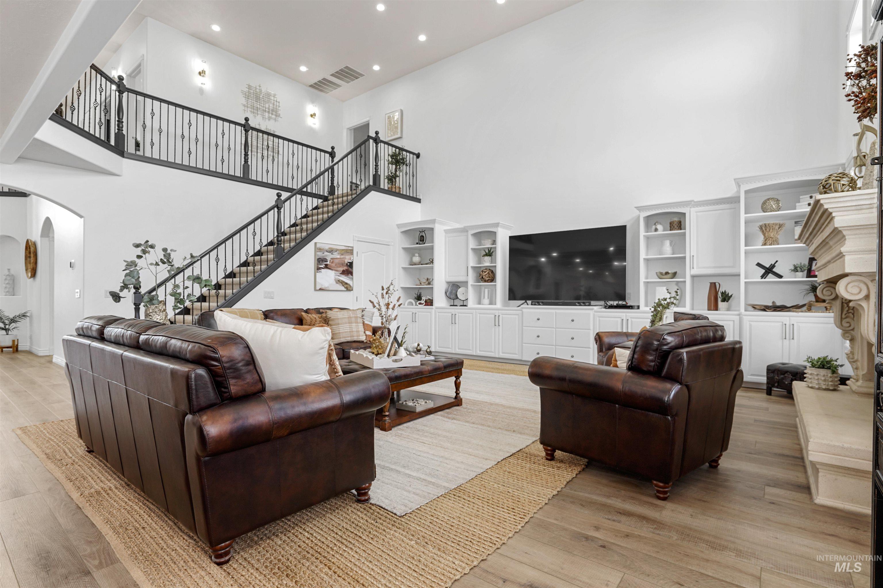 Living room with a high ceiling, recessed lighting, light wood finished floors, arched walkways, and stairway