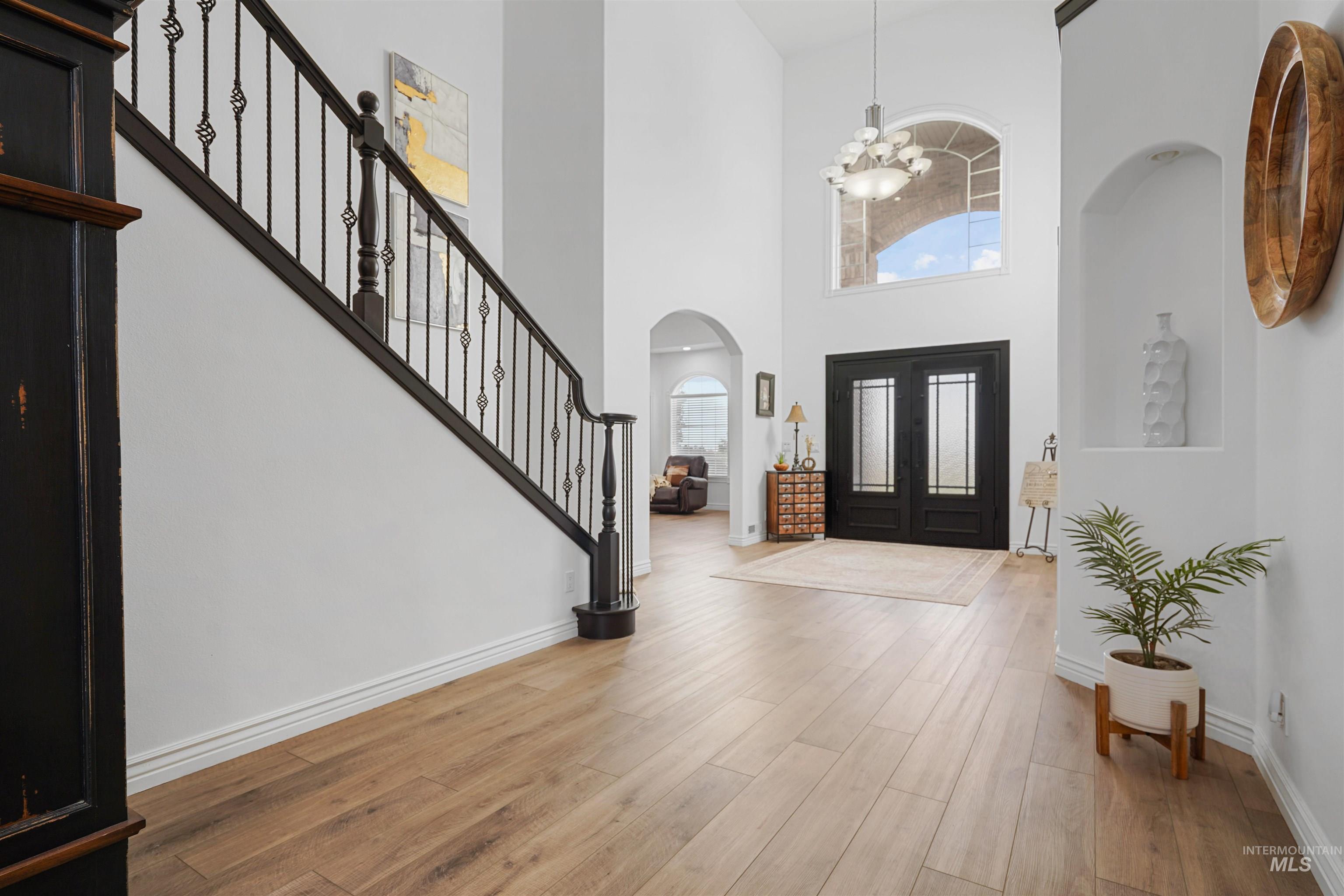 Entryway with stairs, wood finished floors, a chandelier, arched walkways, and a towering ceiling