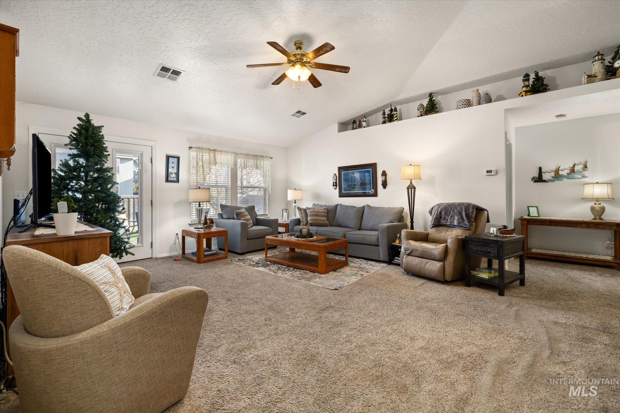 Carpeted living room with a textured ceiling, lofted ceiling, and ceiling fan