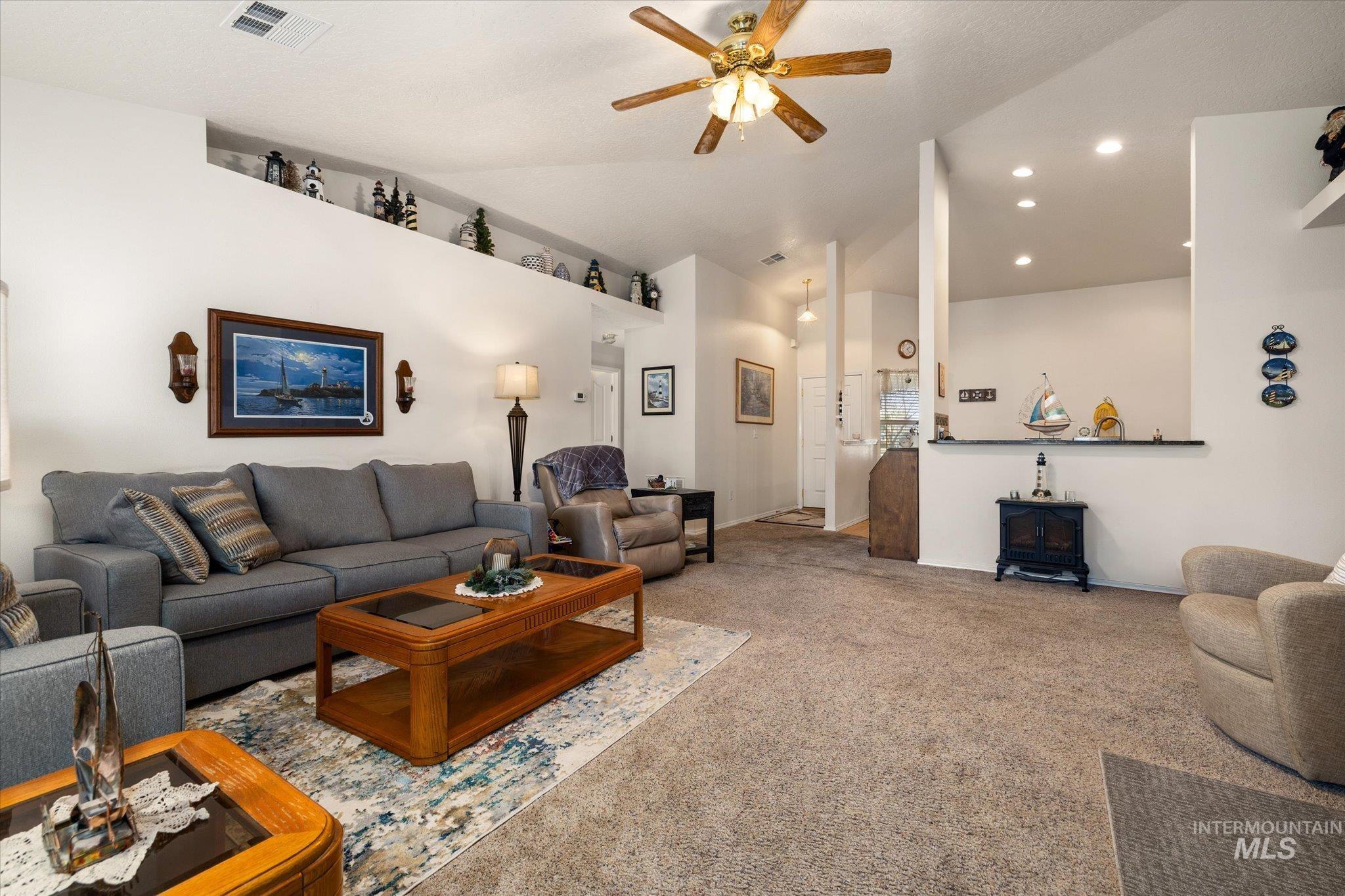 Carpeted living area featuring vaulted ceiling, a wood stove, a ceiling fan, and recessed lighting