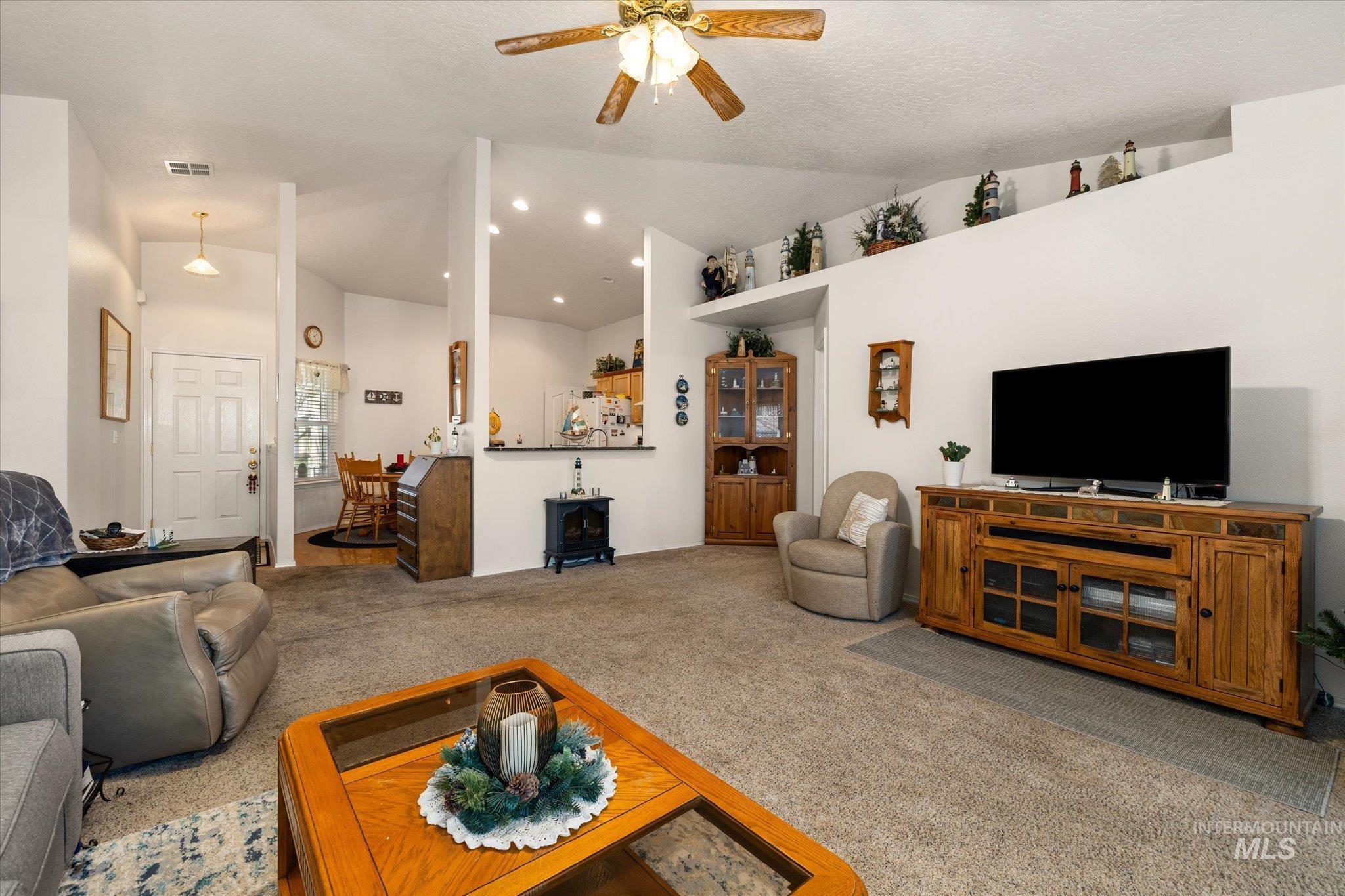 Carpeted living room with a wood stove, ceiling fan, and high vaulted ceiling