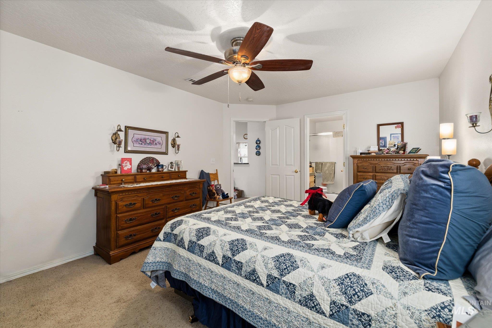 Bedroom with light carpet, ensuite bathroom, and ceiling fan