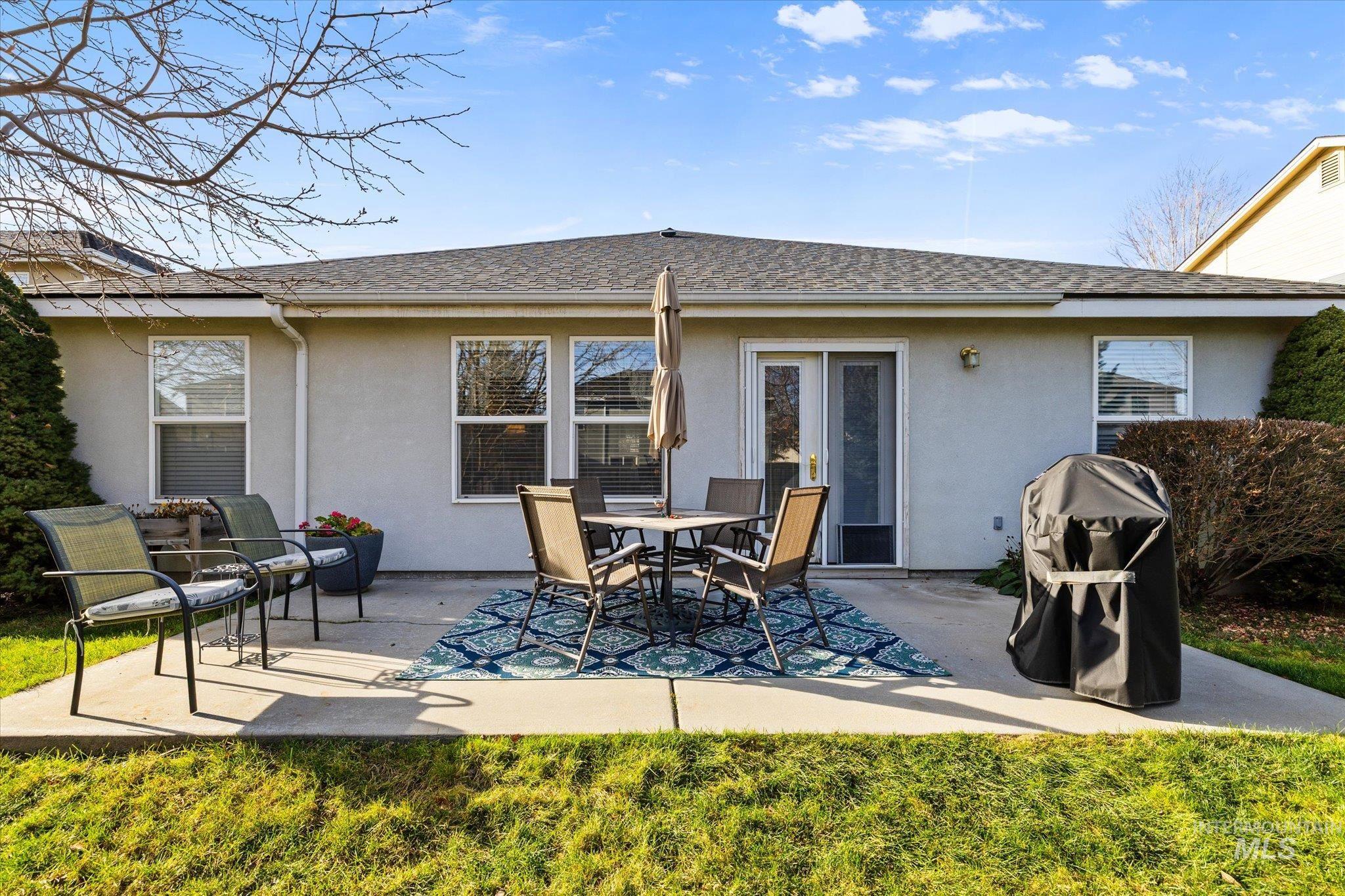 Rear view of property with stucco siding, a patio area, and a shingled roof