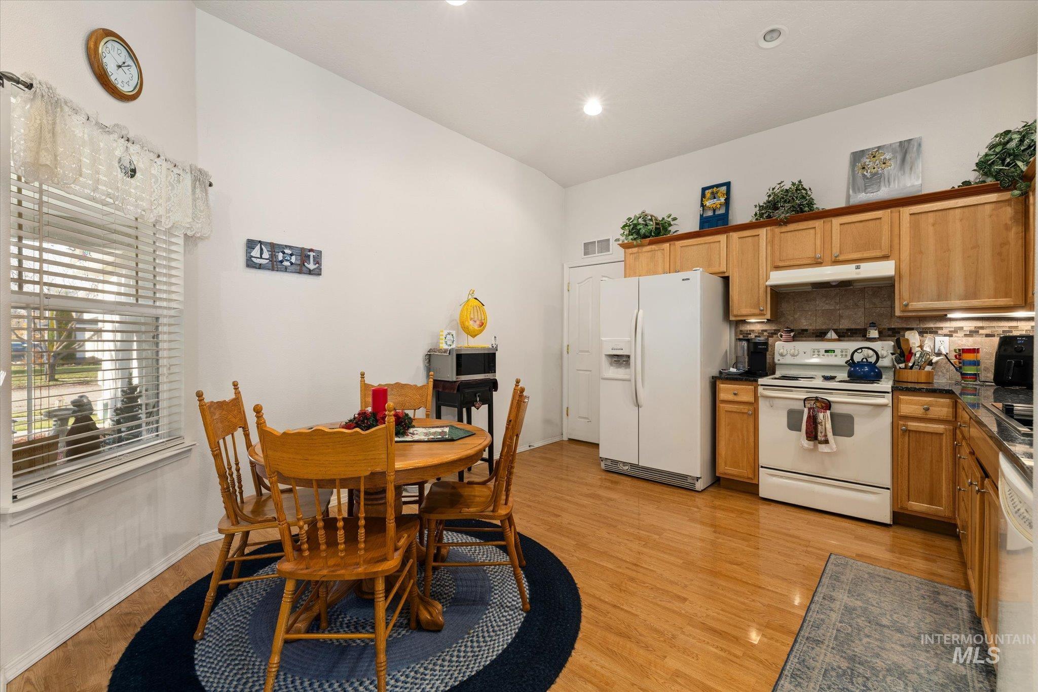 Kitchen with white appliances, lofted ceiling, brown cabinets, backsplash, and under cabinet range hood