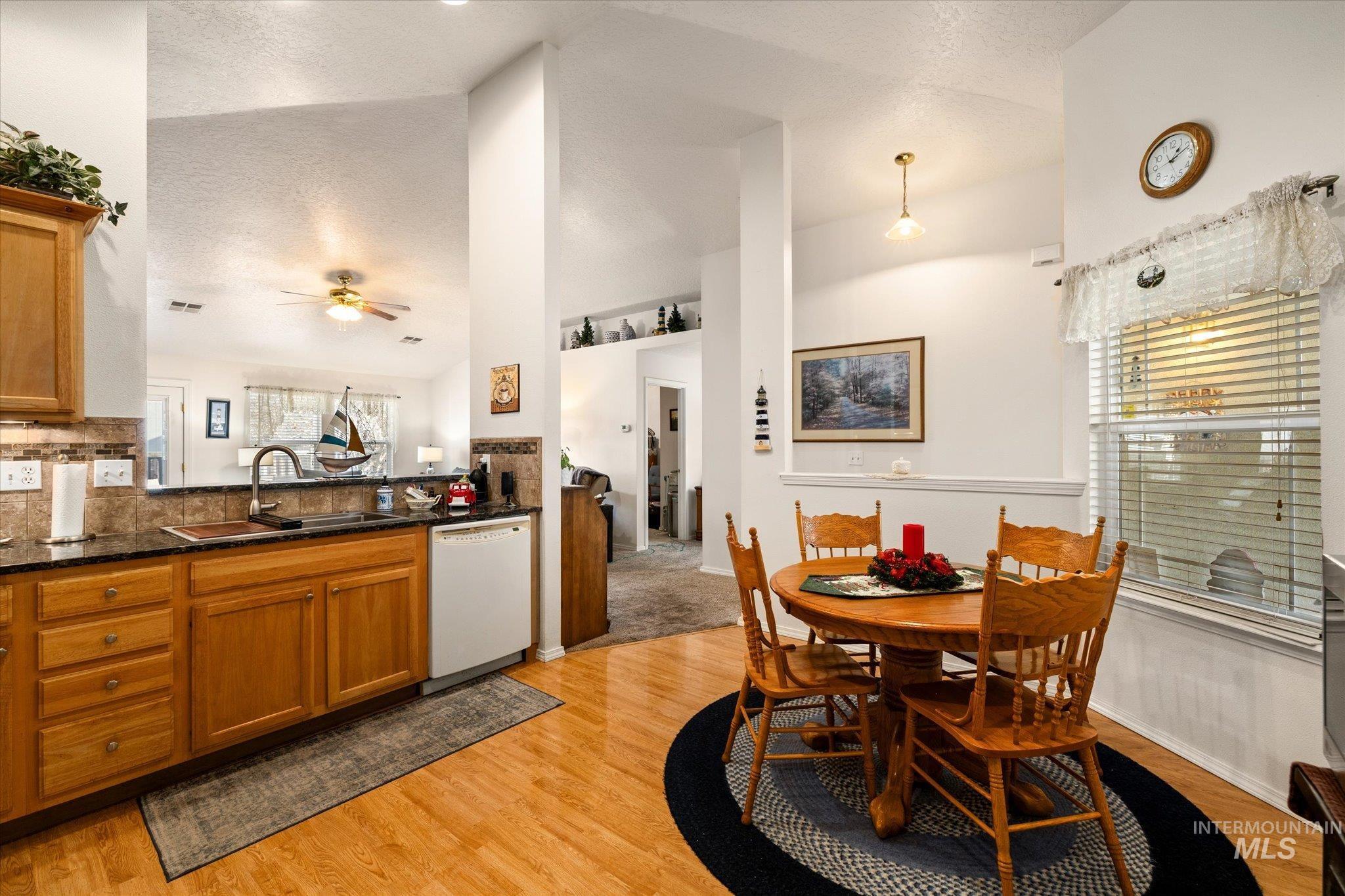 Kitchen featuring brown cabinets, dark stone counters, white dishwasher, light wood-type flooring, and ceiling fan
