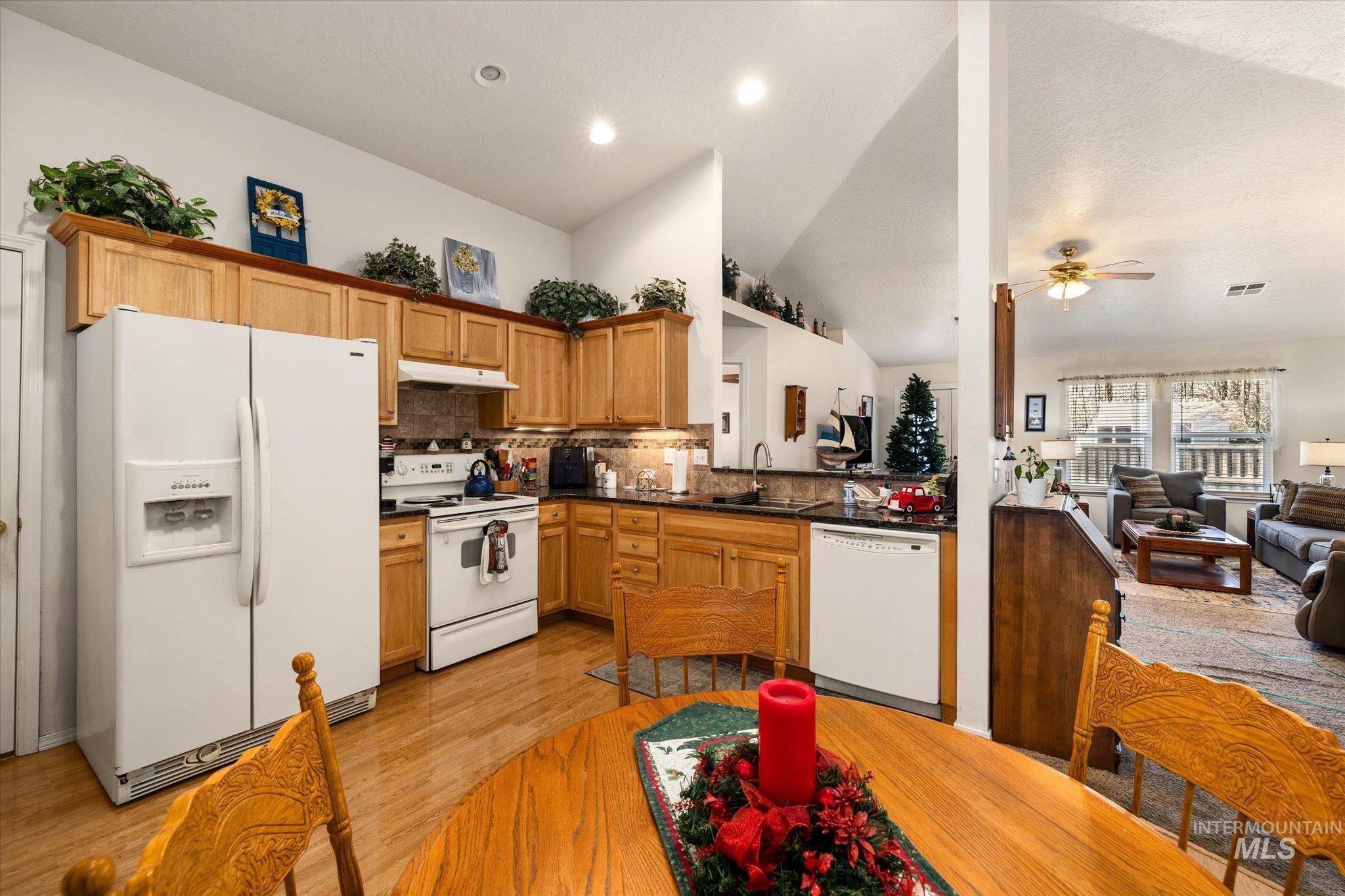 Kitchen featuring white appliances, open floor plan, light wood finished floors, decorative backsplash, and brown cabinetry